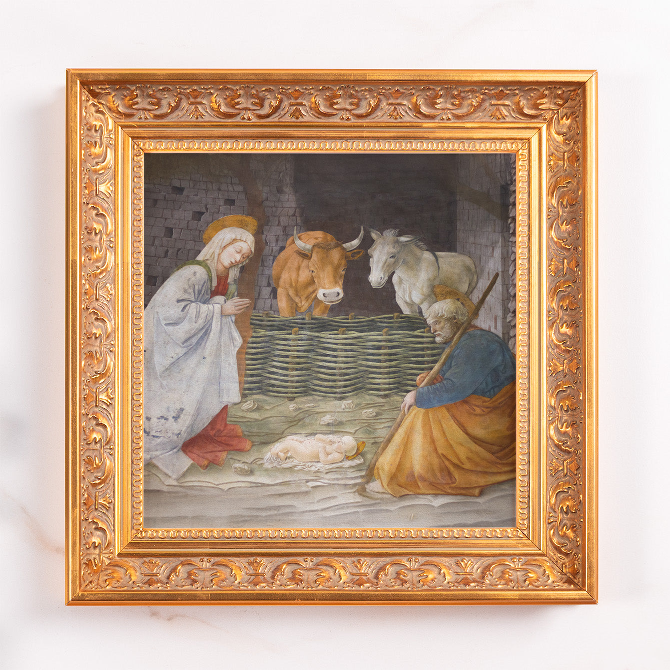Framed Nativity art print in golden wood tone with ornate detailing; Mary, Joseph, and animals watching baby Jesus.