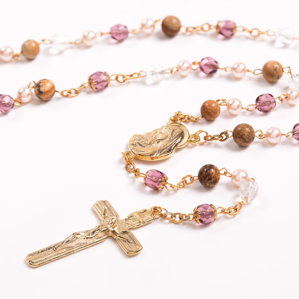 Close-up of a golden rosary with a crucifix, mother Mary medal, brown, pink, and clear beads, and golden chain links for prayer.