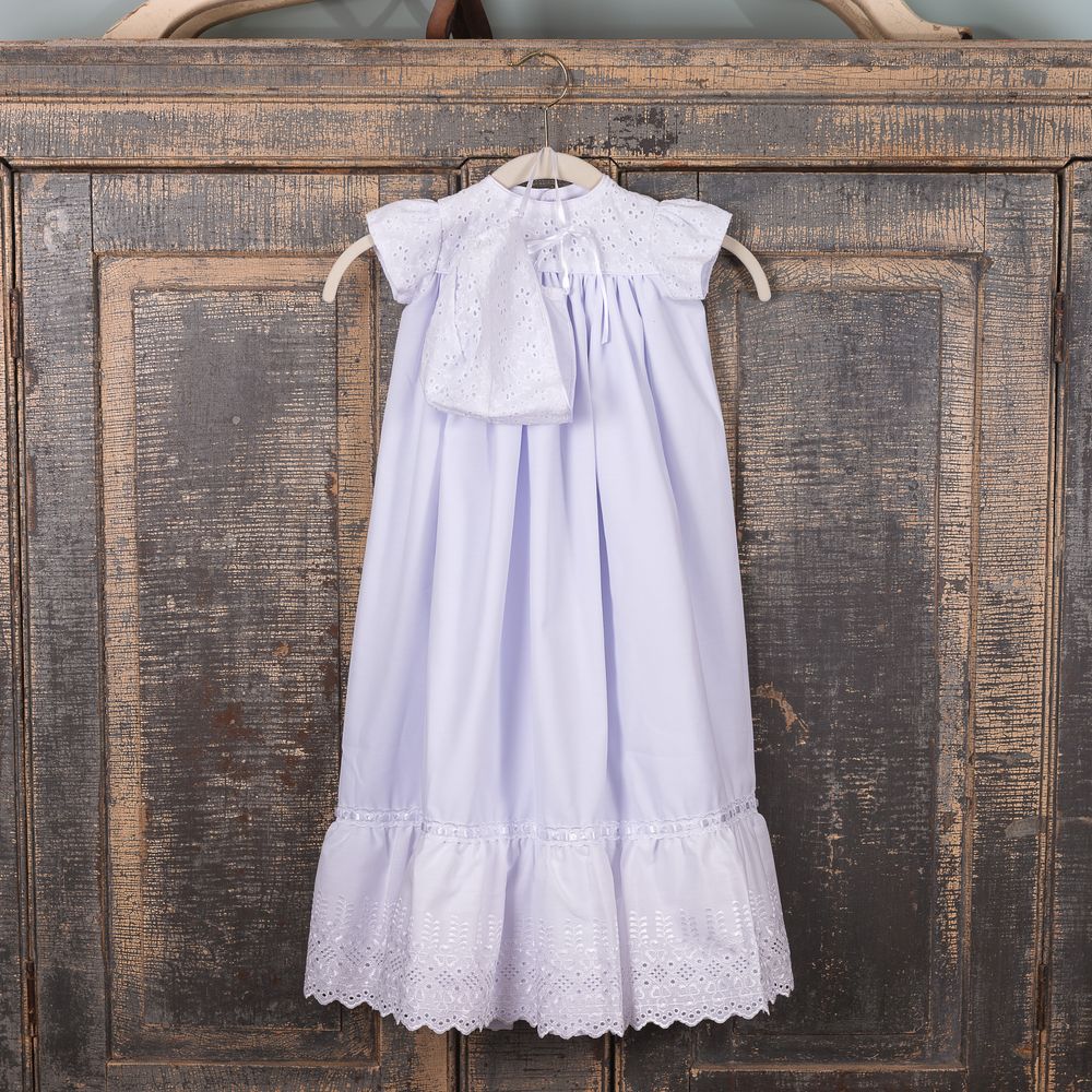White cotton baby gown with eyelet trim and matching bonnet on hanger.