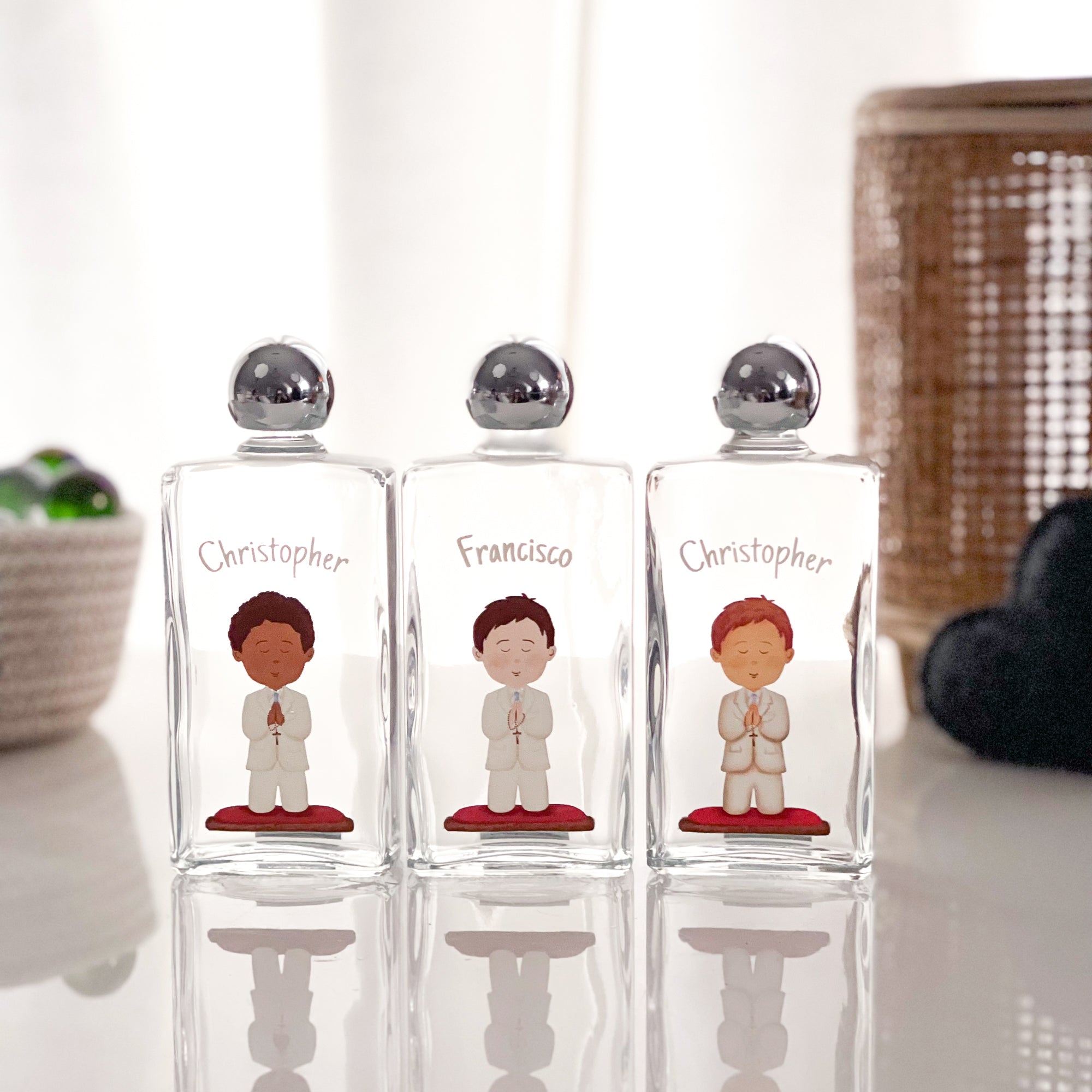 Personalized, clear glass favor bottles with metal lids, decorated with praying boy graphics for religious events.