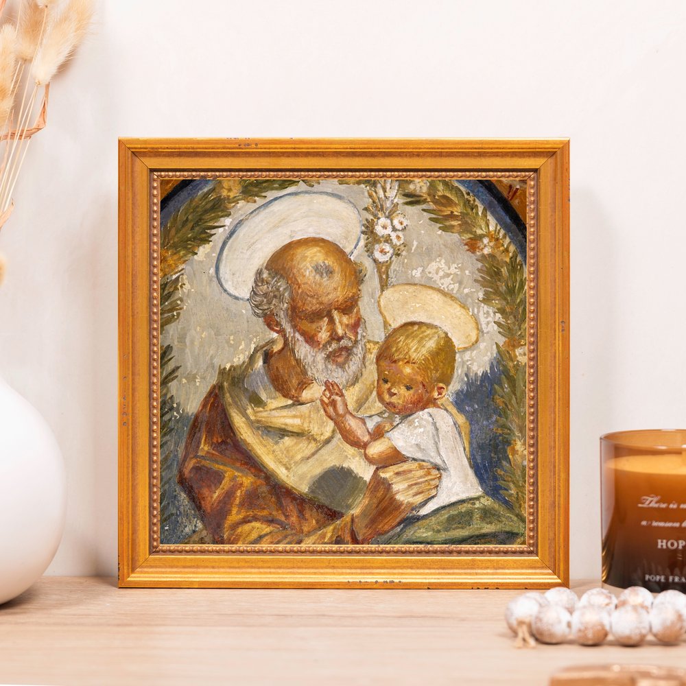 Framed, Religious oil painting of Saint Joseph and Baby Jesus in a gold frame on a shelf.