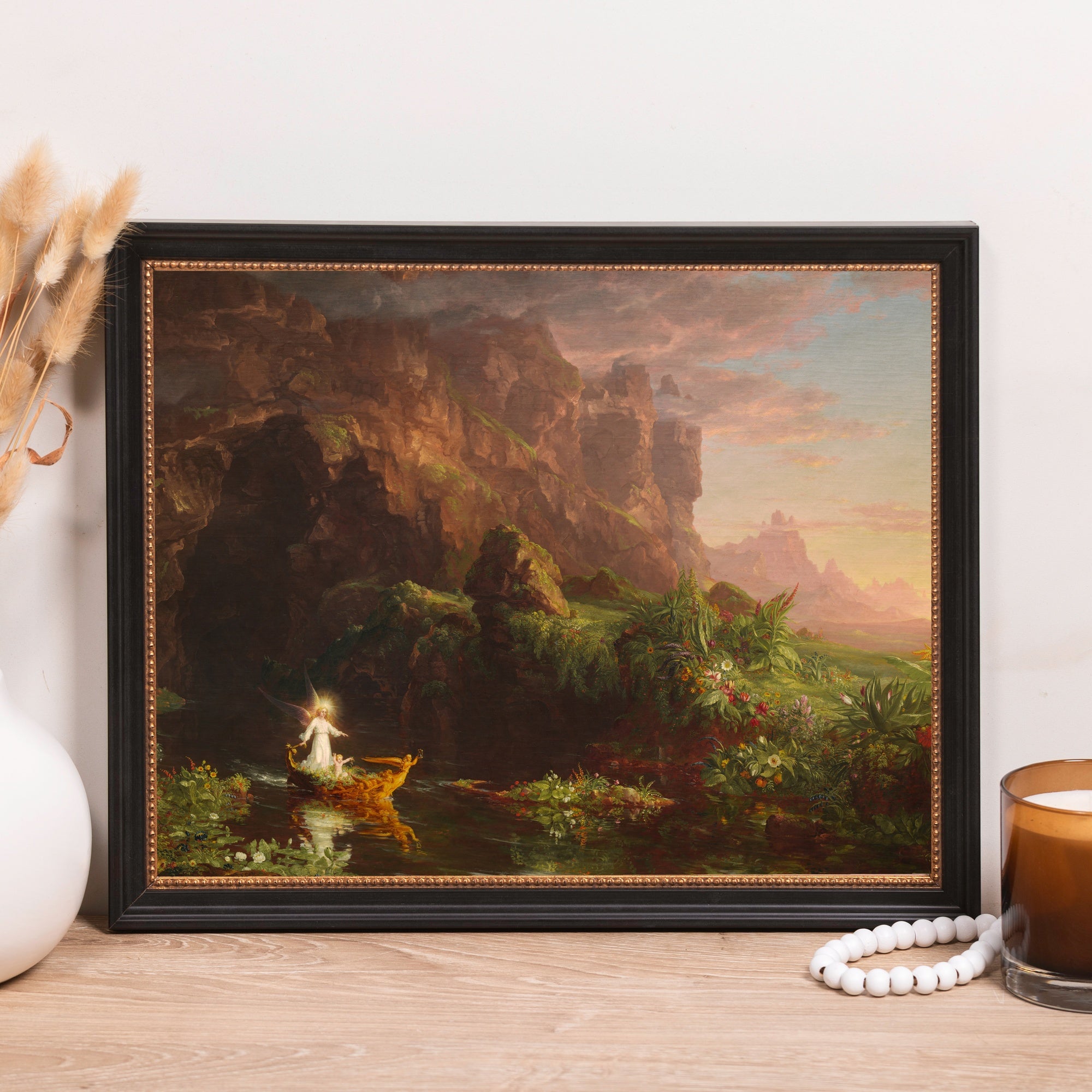 Framed print of idyllic landscape with angel in boat, set in black ornate frame.