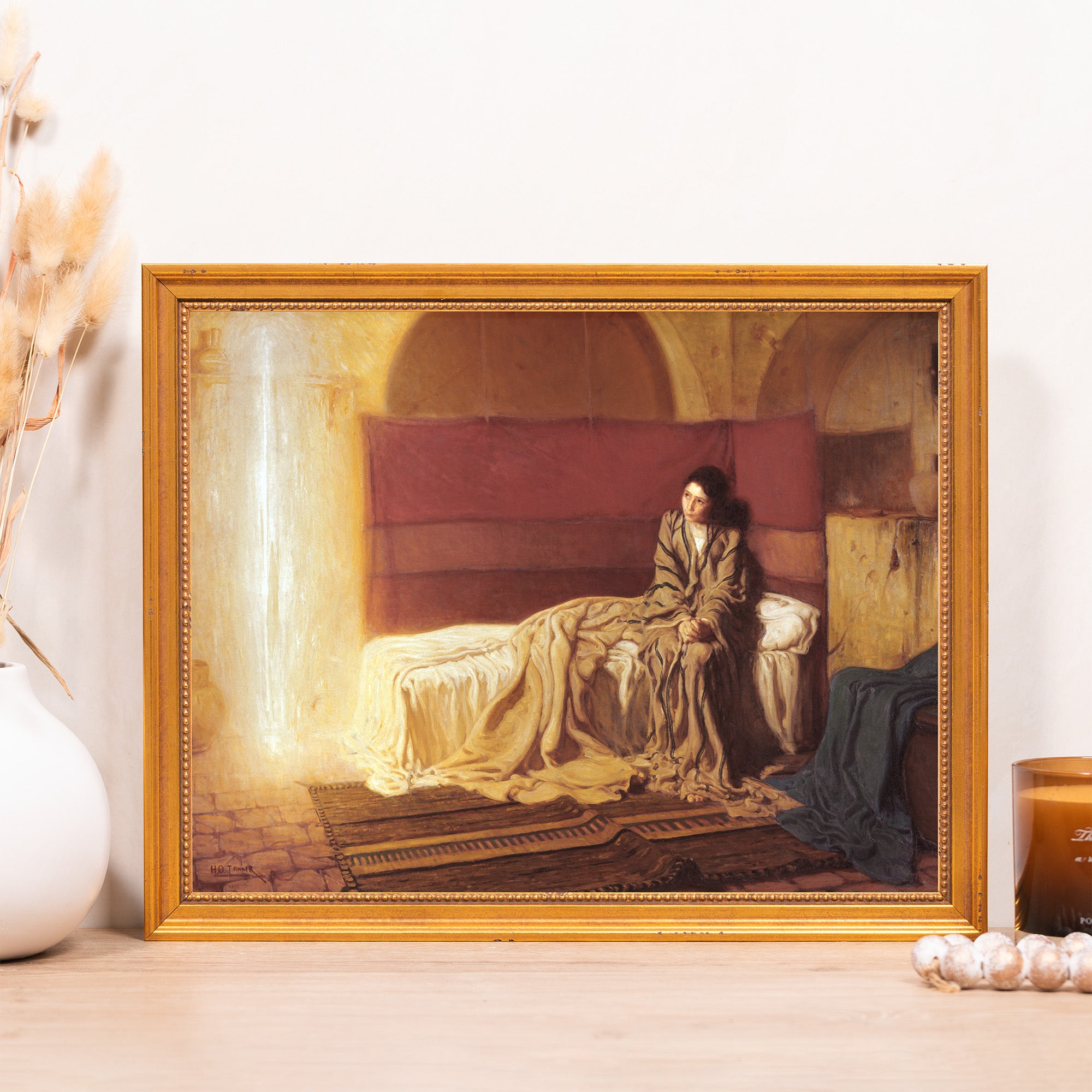 Framed painting of a woman sitting on a bed, with a gold frame and dark background.