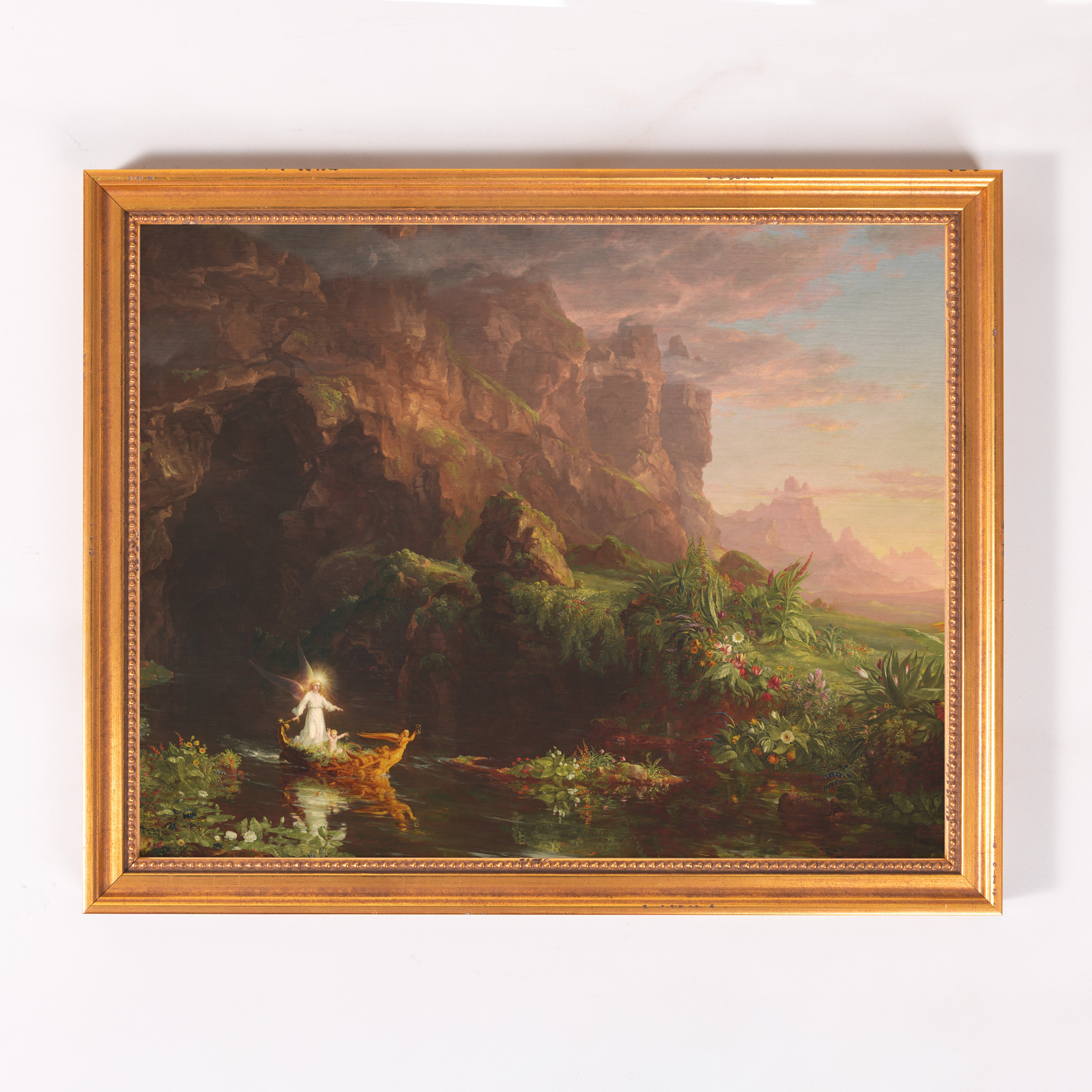 Framed Oil painting depicts a river landscape with a radiant figure in a boat, surrounded by lush vegetation, framed in gold.