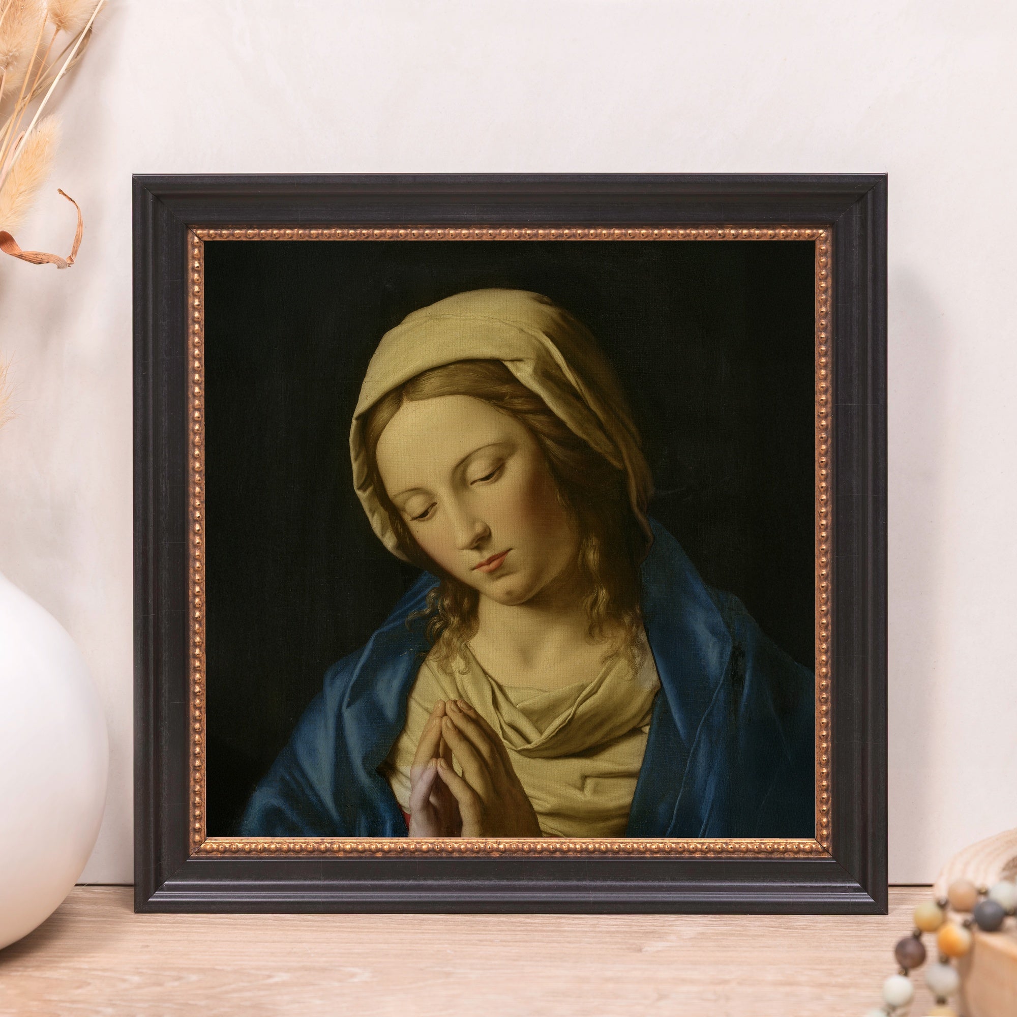 Framed canvas print of Mary praying with a blue shawl in a black frame with gold beading.