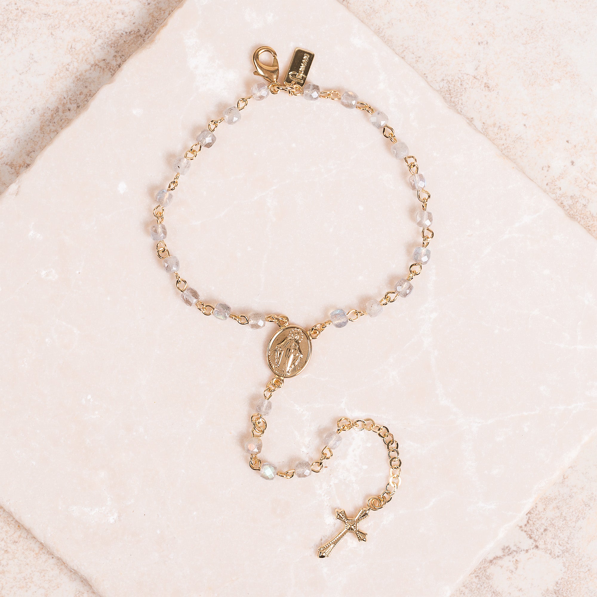 Gold, gray rosary bracelet with beads and a cross charm on a square stone.