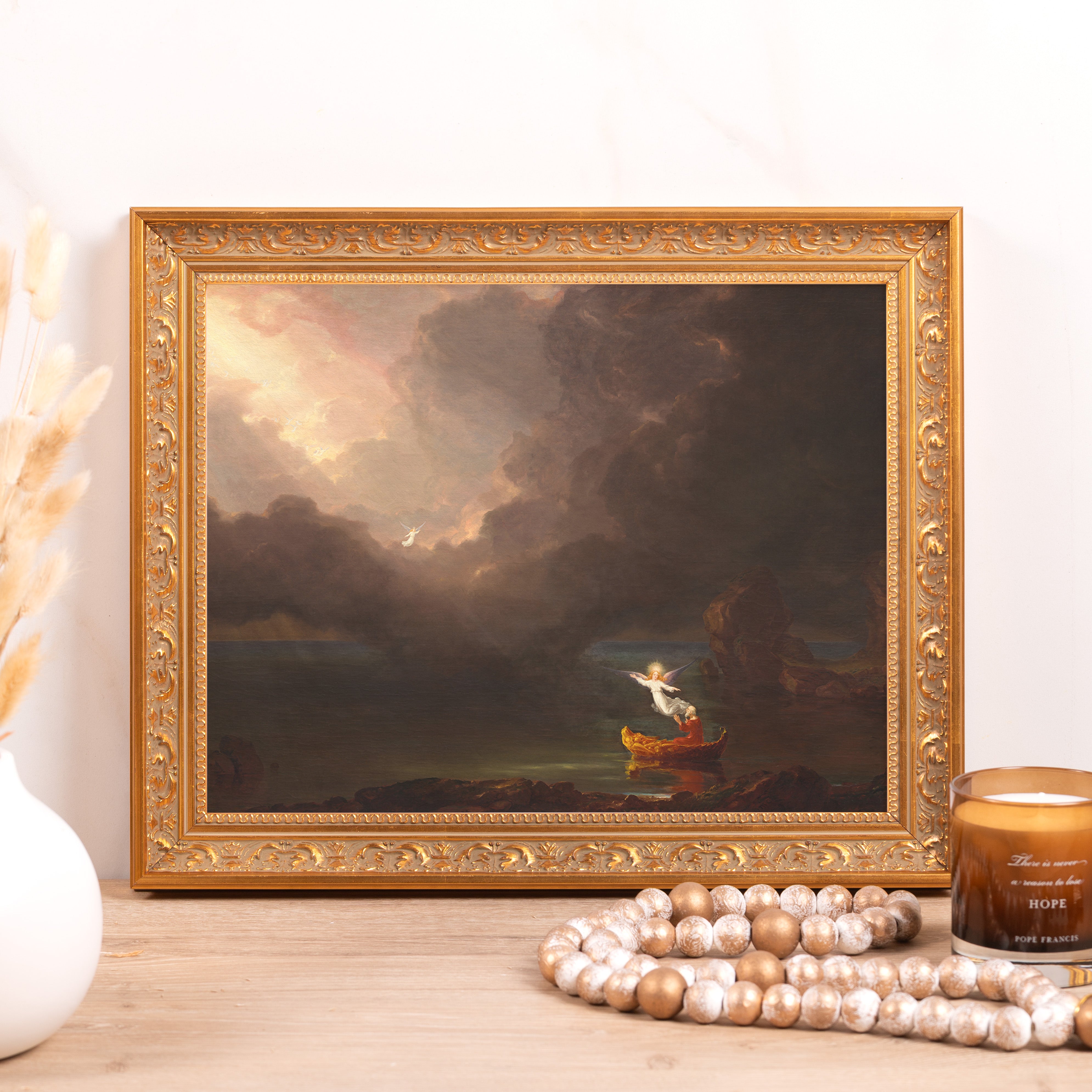 Framed art depicts an angel guiding a boat in a dark landscape, gold ornate frame.