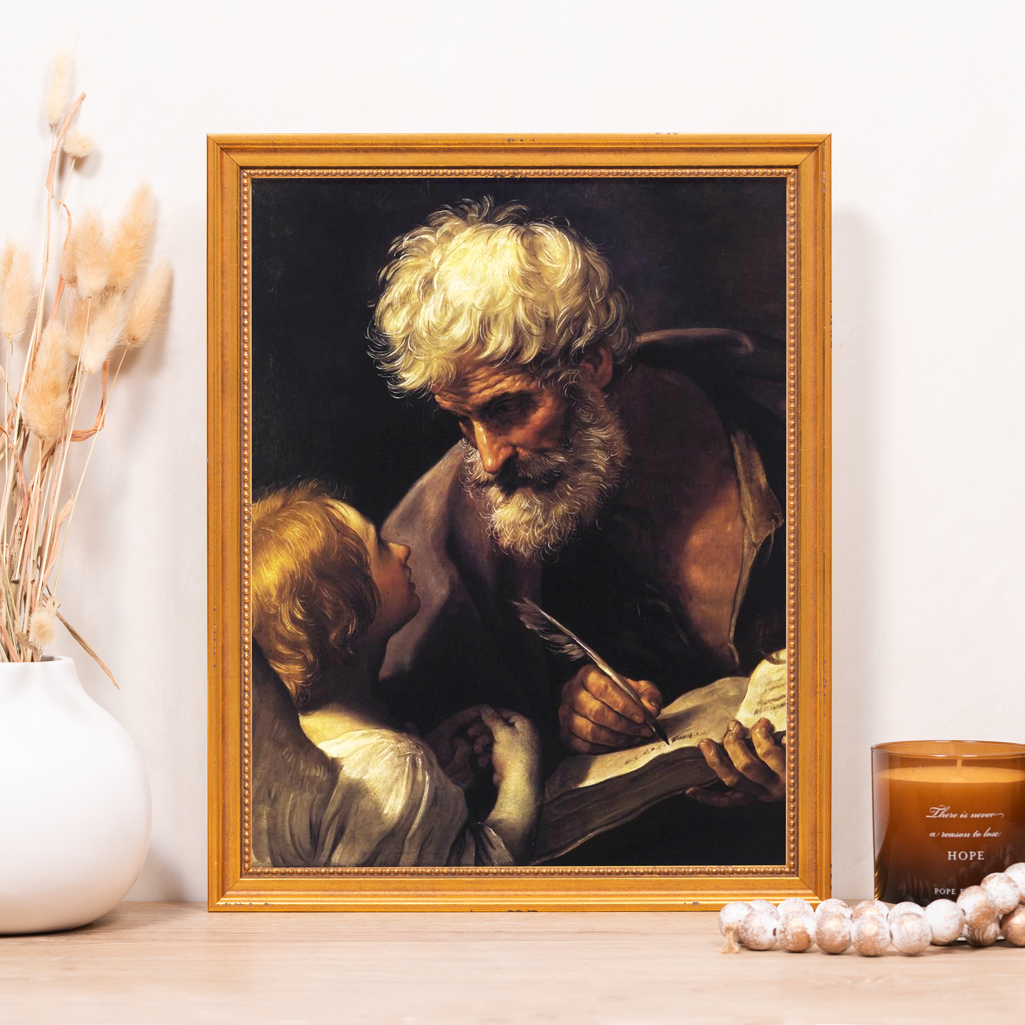 Framed print depicts an older man writing while a child looks on; the frame is gold.