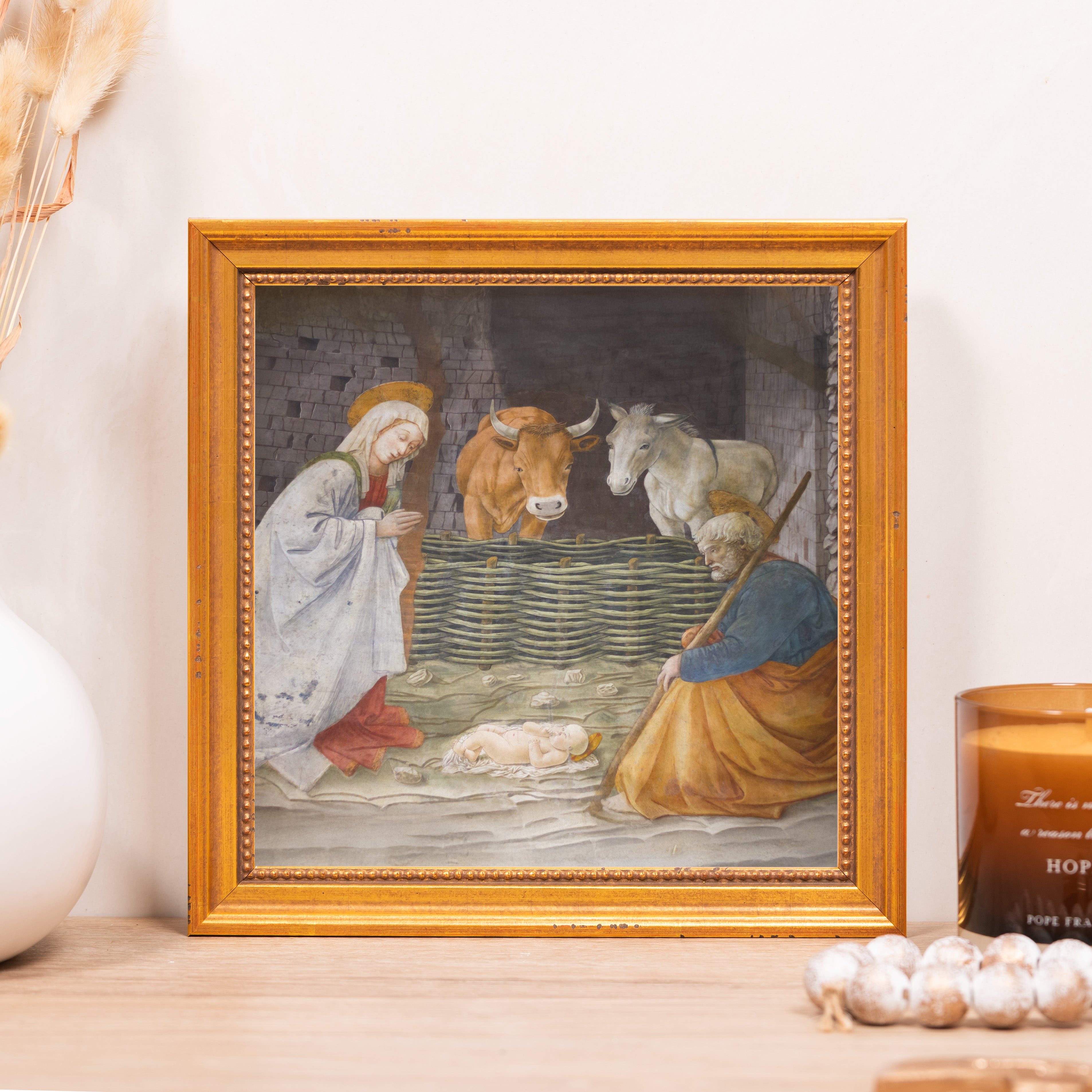 Framed Nativity art print. Golden frame, depicts Mary, Joseph, and baby Jesus in a stable with a cow and donkey.
