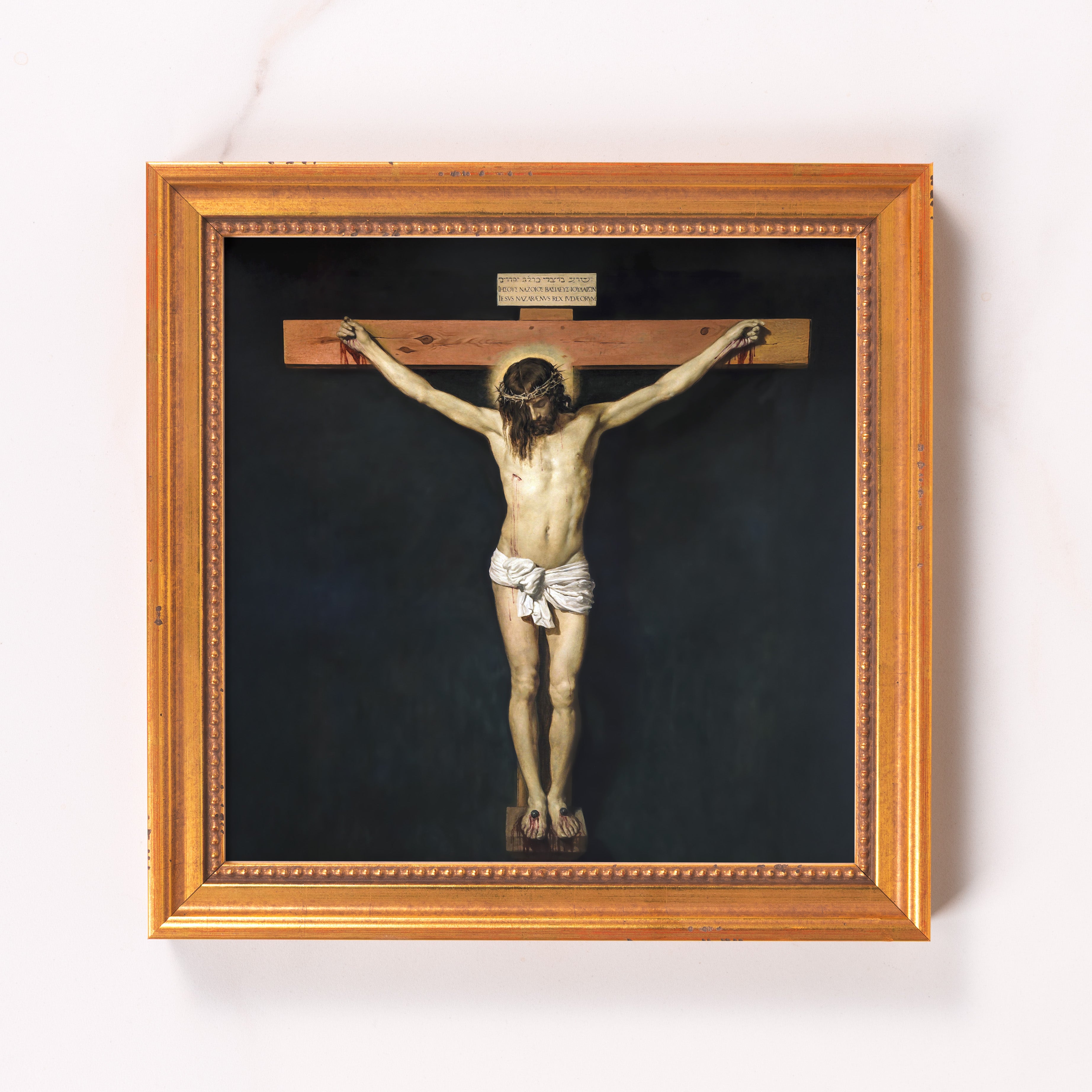 Framed painting of the crucifixion, featuring Jesus on the cross against a dark background, with an ornate gold frame.