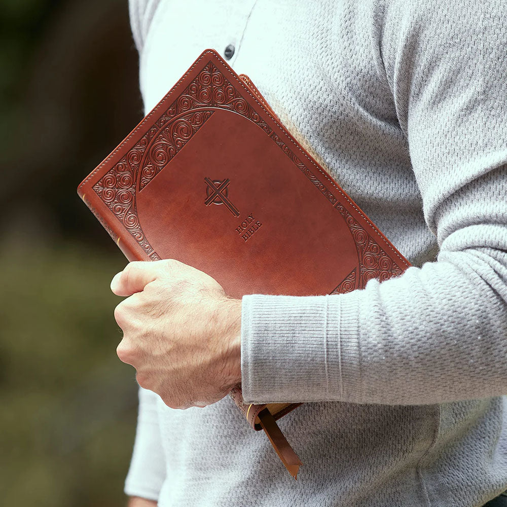 Person holding a brown, leather-bound Bible with embossed cross and floral details on the cover.