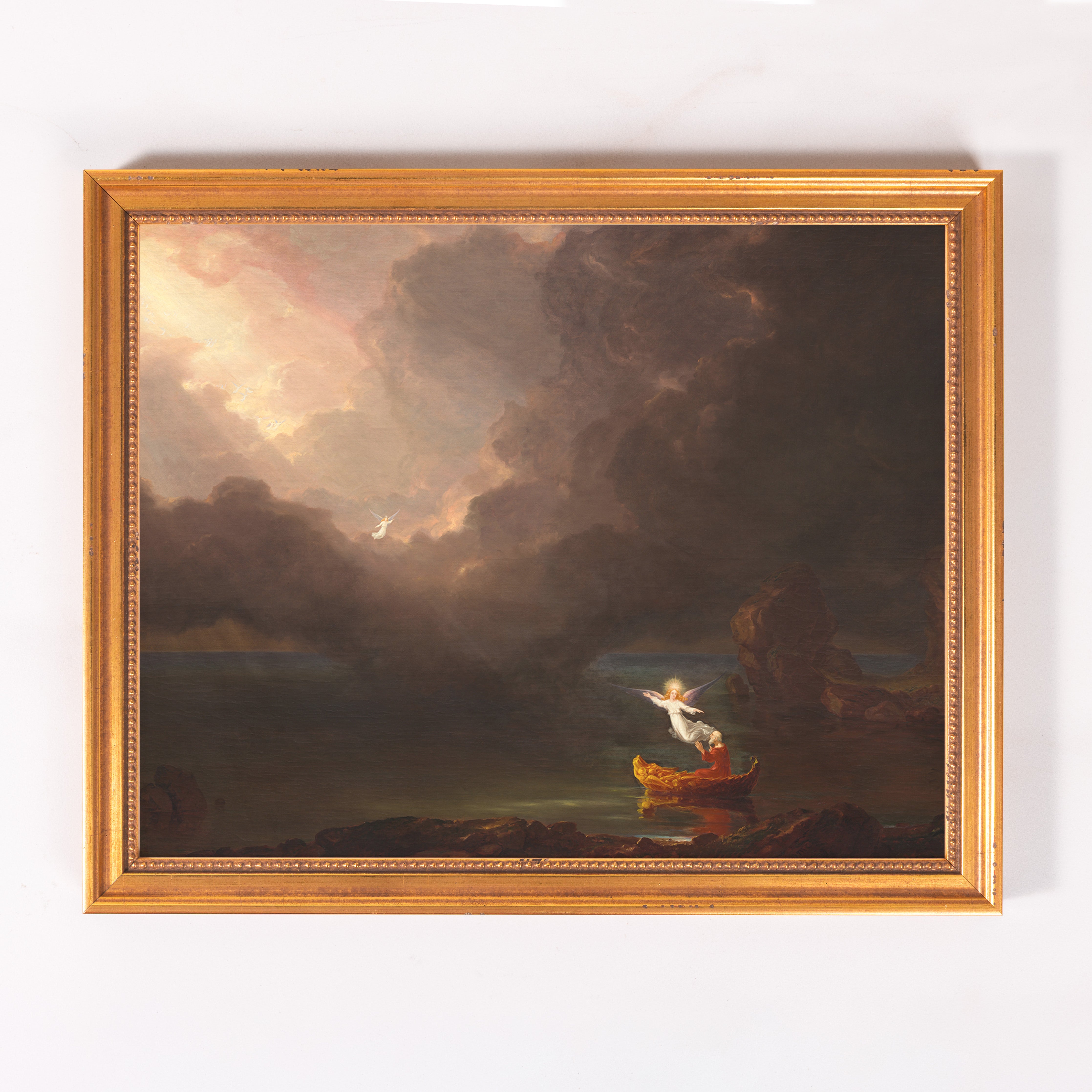 Framed Painting depicts a dark, moody seascape, with an angel and figure in a boat, in a gold frame.