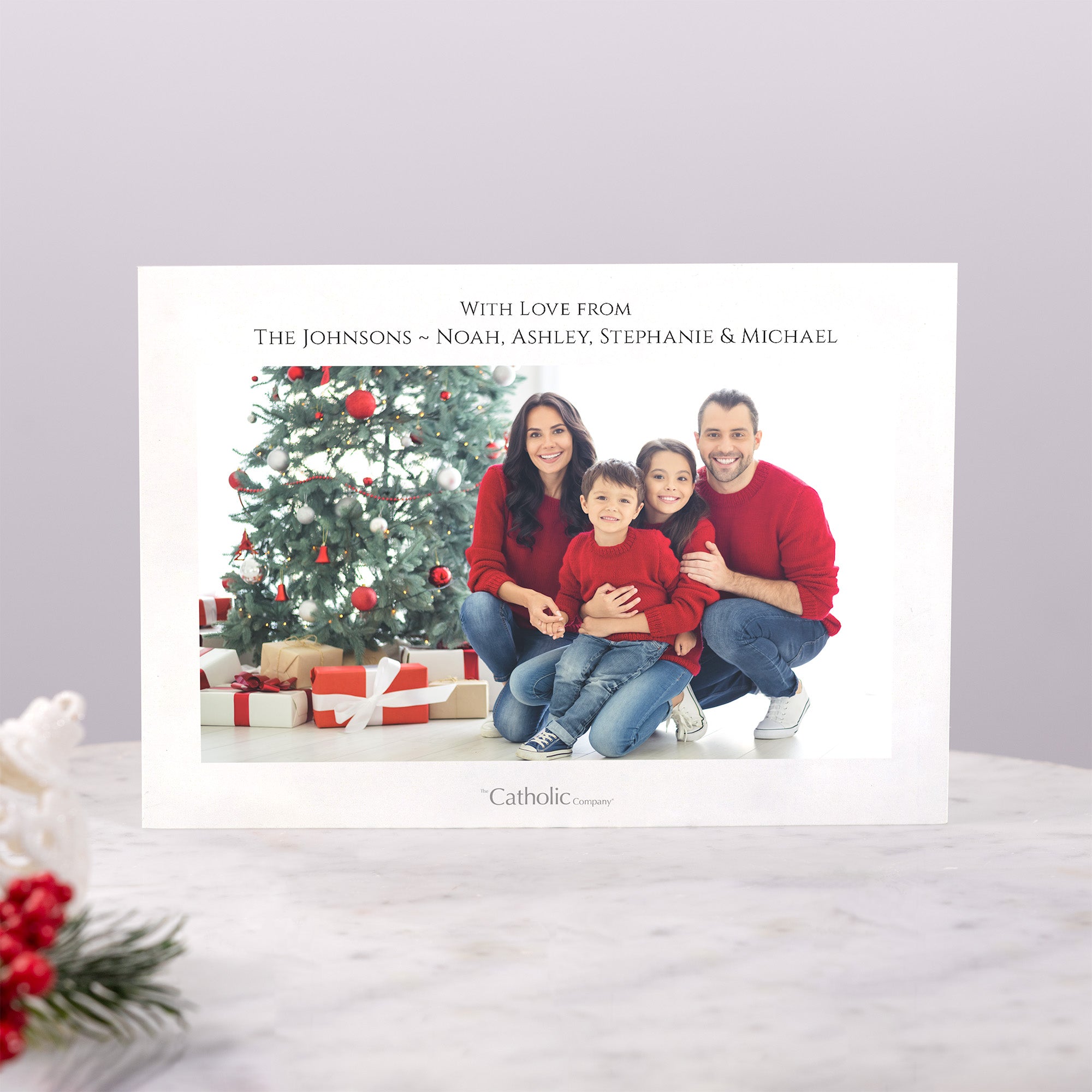 Family Christmas card featuring a family of four smiling by a tree with gifts.