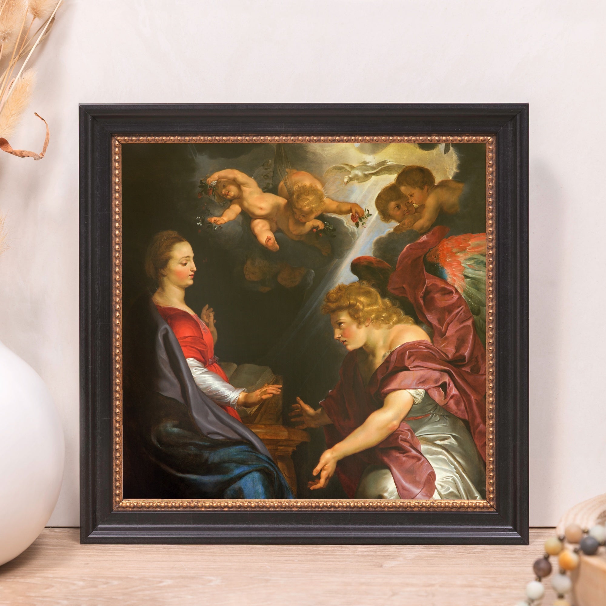 Framed painting of the Annunciation scene with Mary, an angel, and cherubs in a dark, baroque style.