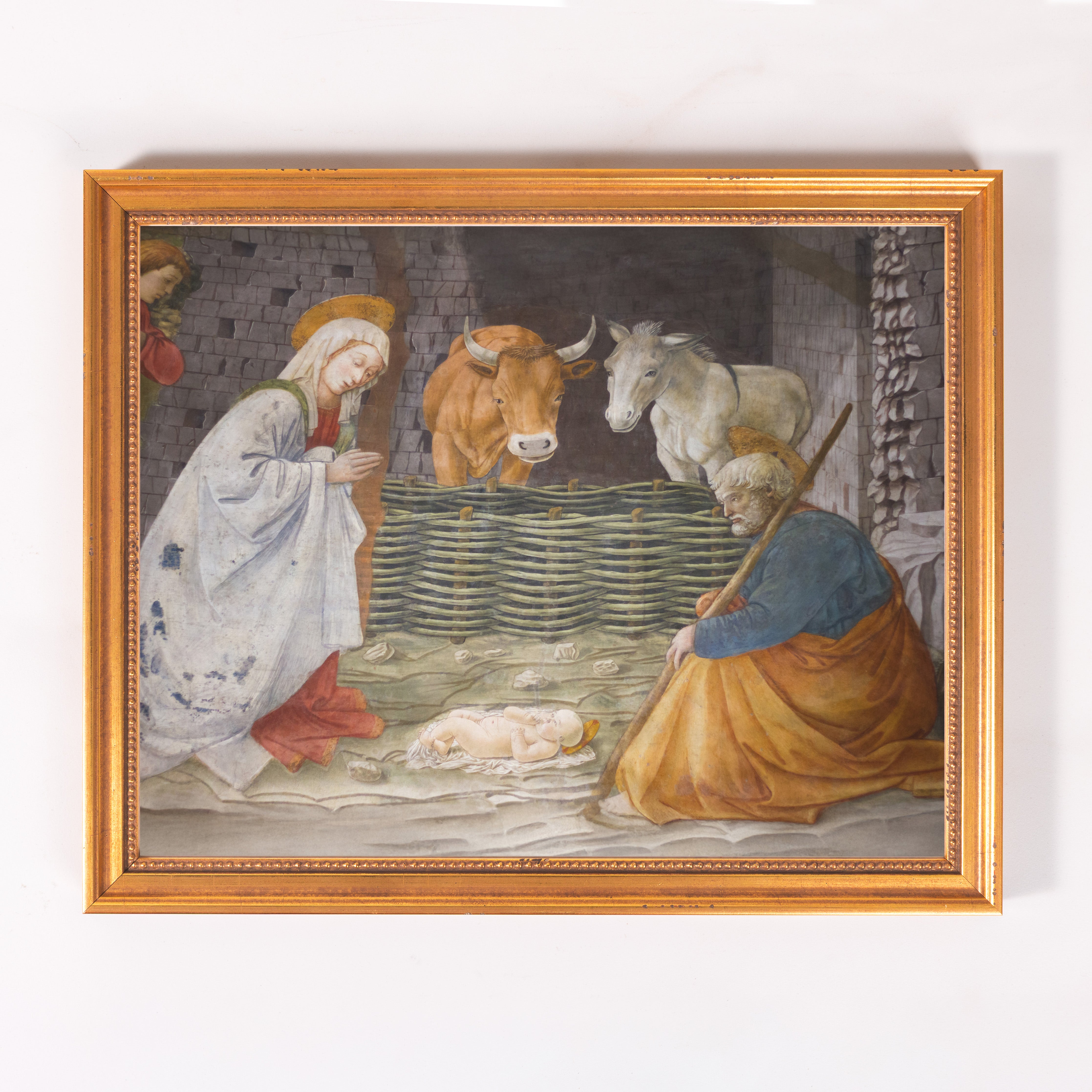 Framed painting of the Nativity scene with Mary, Joseph, Jesus, and animals in soft colors with a gold frame.