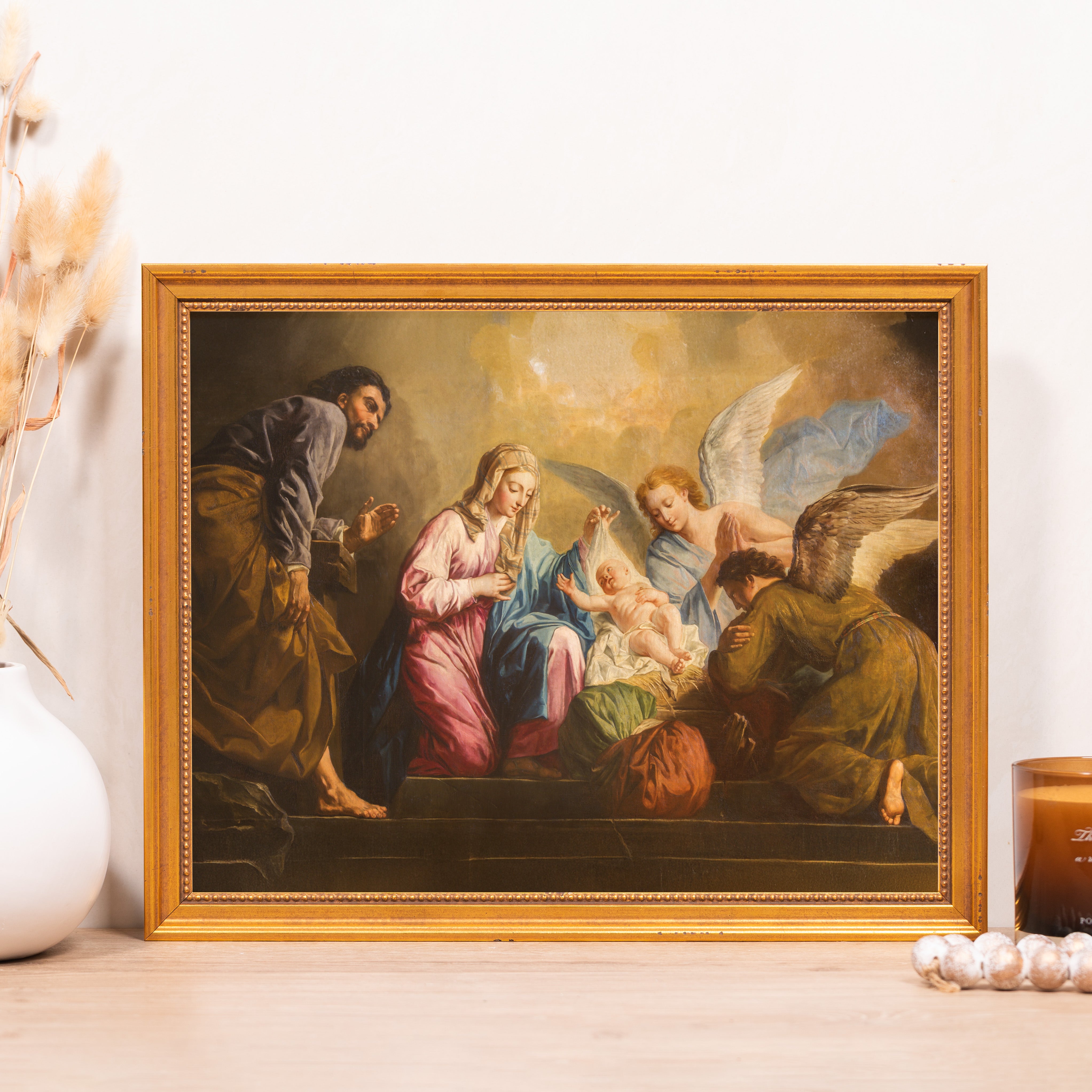 Framed painting of the Nativity with Joseph, Mary, angels, and baby Jesus in gold frame.
