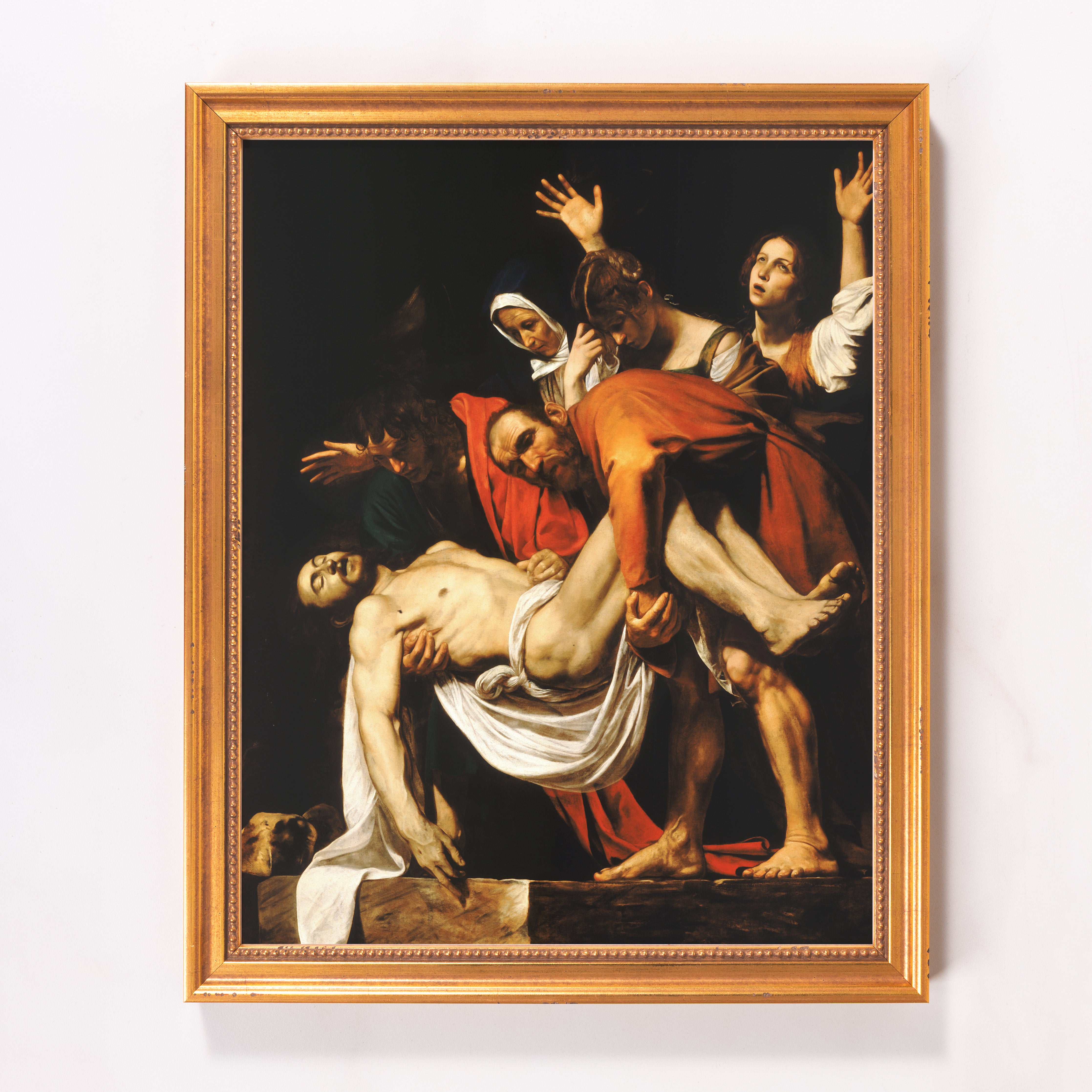 Framed Caravaggio print showing the Entombment of Christ with black background and gold frame.