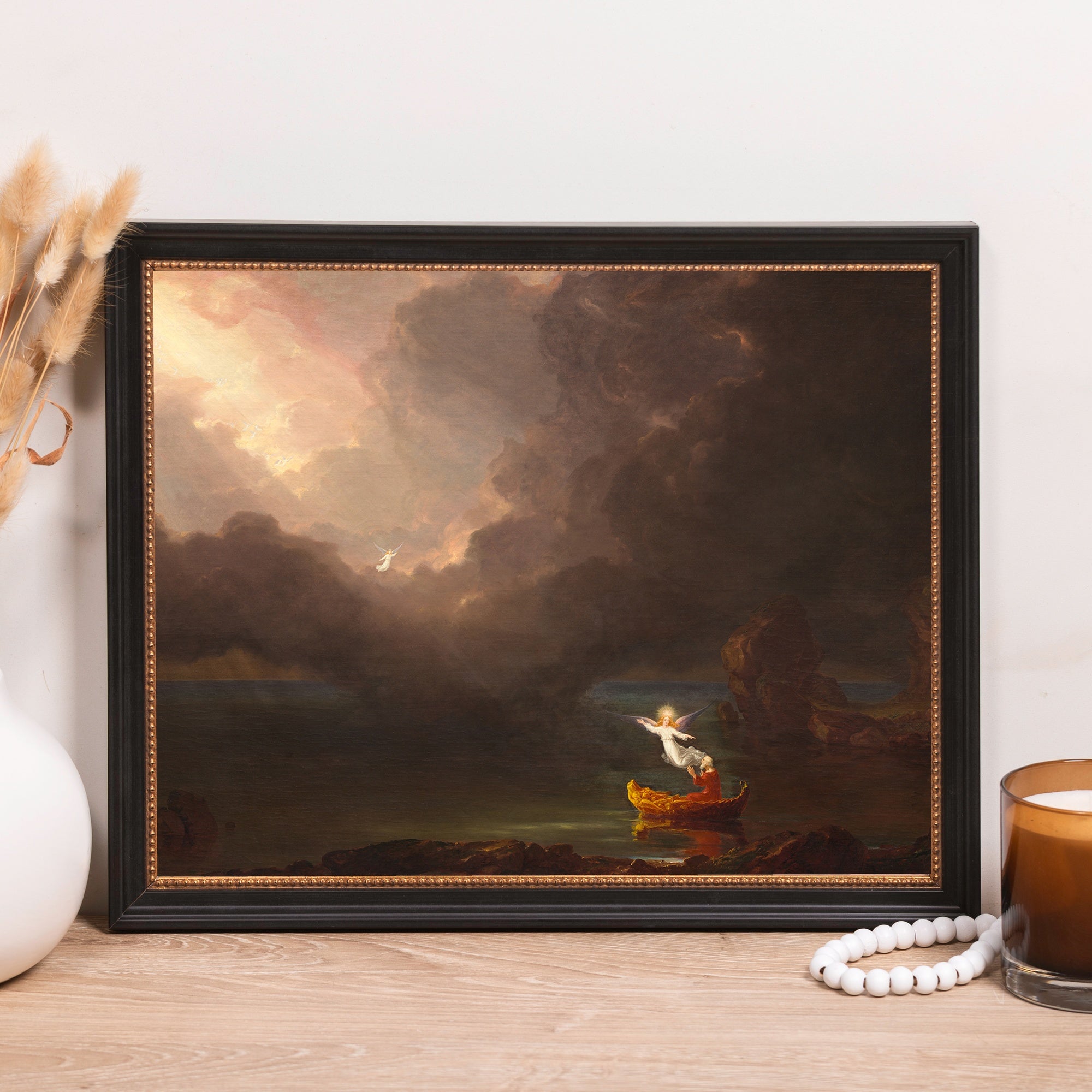 Framed painting depicts angels on a boat surrounded by a dark sky with bright light breaking through.