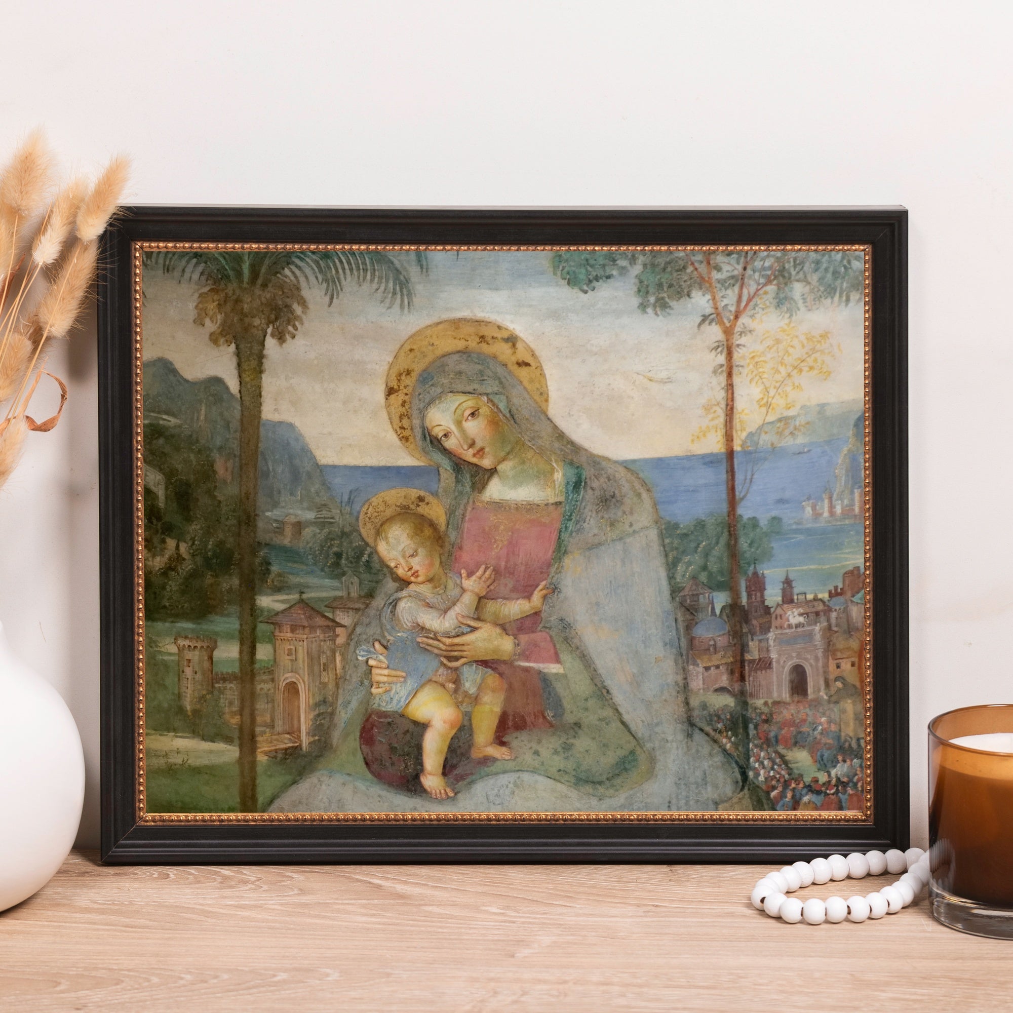 Framed art print of Madonna and child with landscape background in black frame.