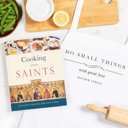 Cookbook titled 'Cooking with the Saints' on a kitchen counter with a cutting board, bowl of green beans, and lemon.
