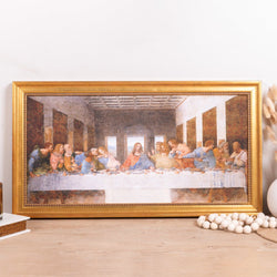 Framed print of The Last Supper in a gold ornate frame, displayed on a wooden surface.