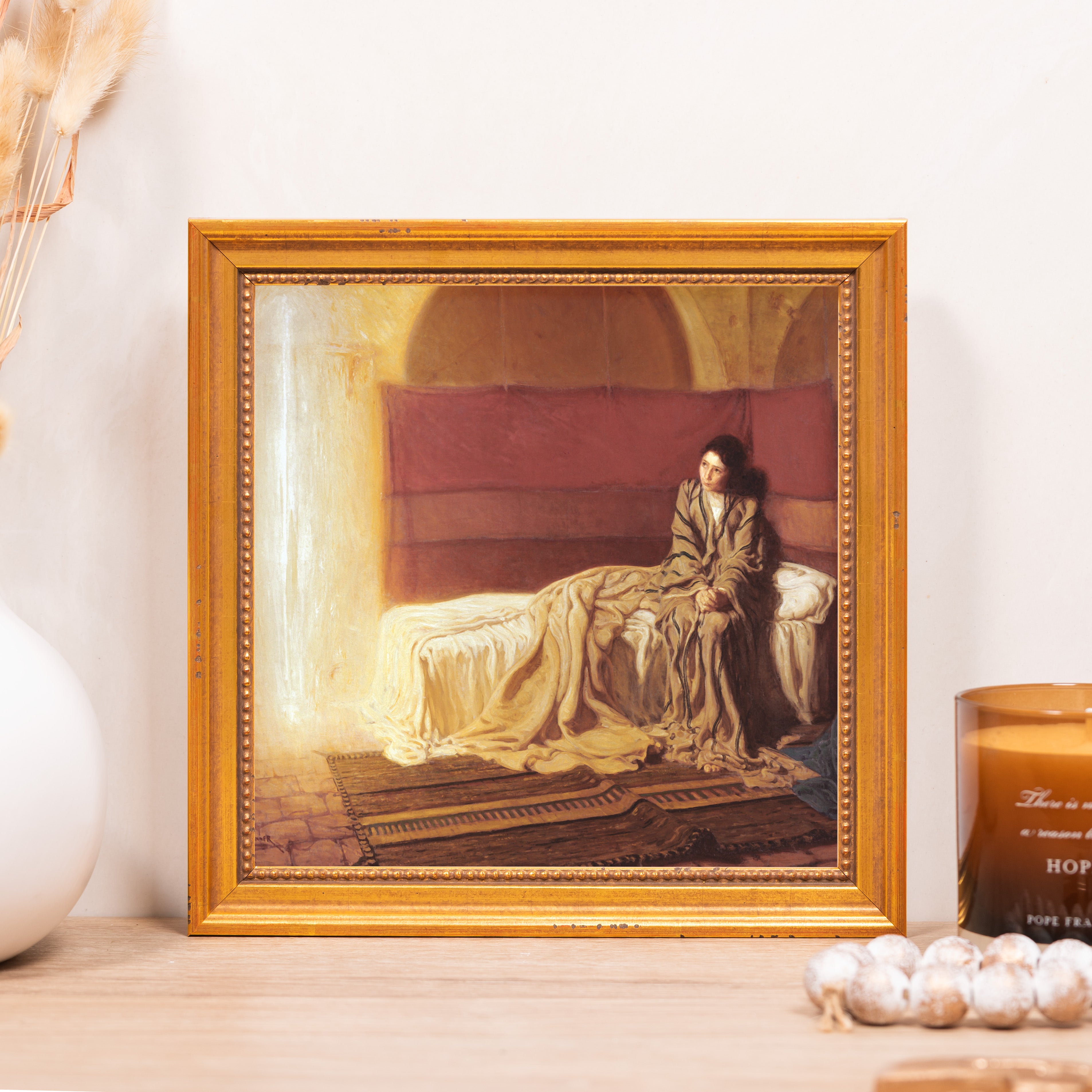 Framed art print depicts a woman sitting on a bed, with a gold-tone frame and textured finish.