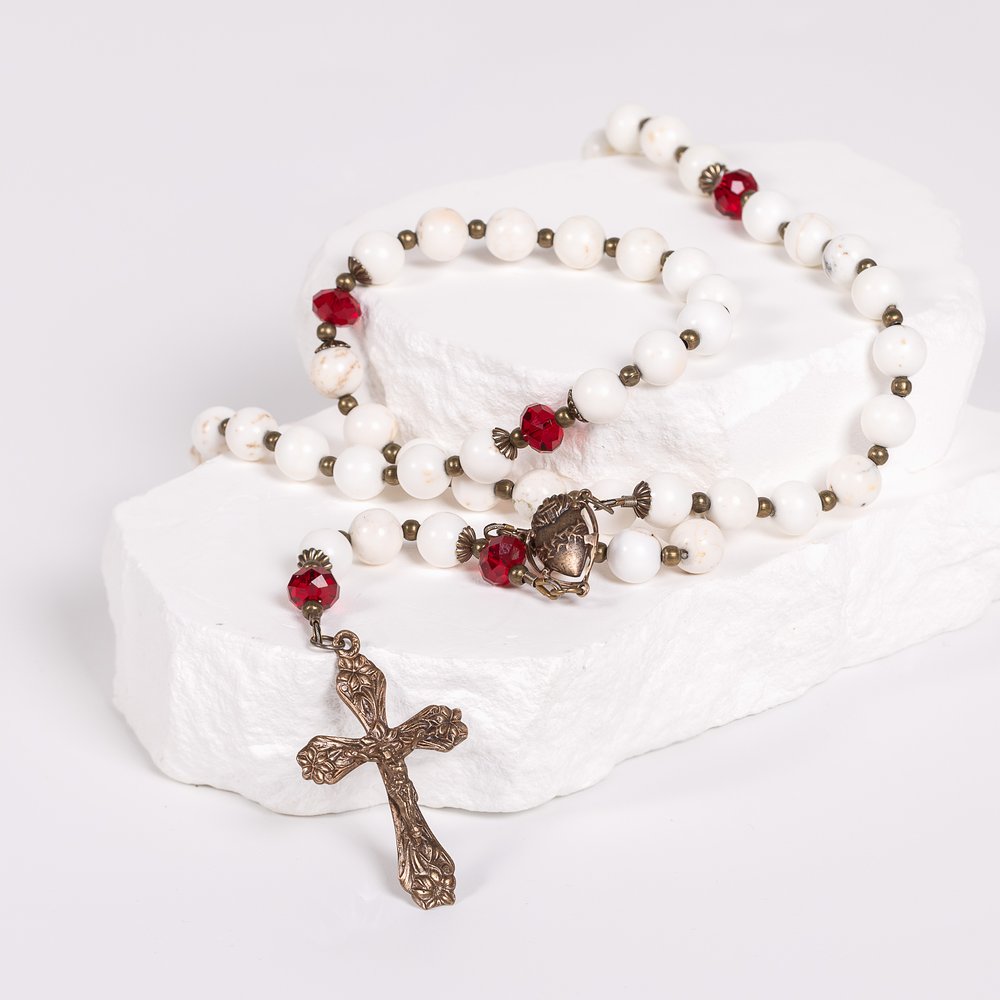 Rosary with white beads, red accents, and a bronze cross on a white surface.