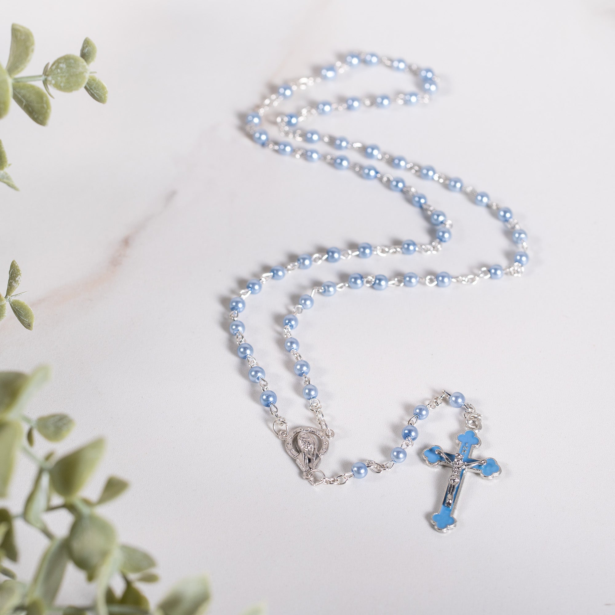Blue rosary with silver chain and cross on a white marble surface.