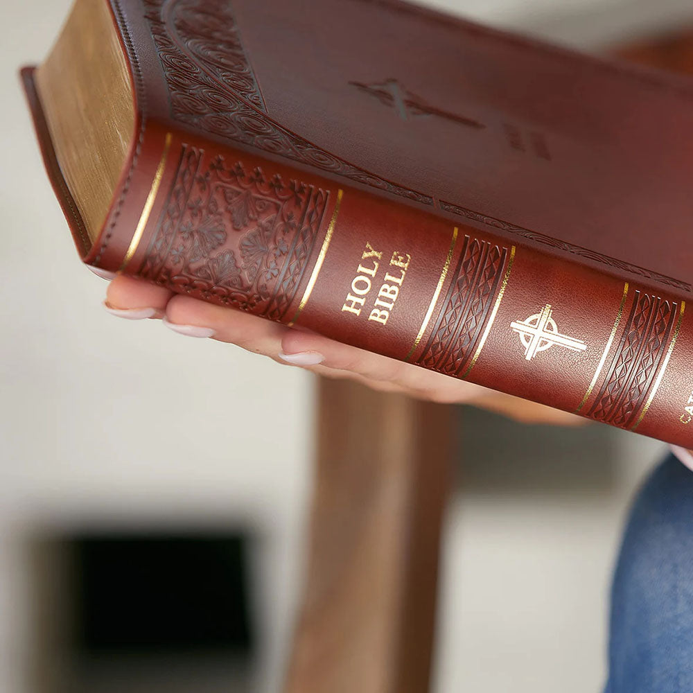 Holy Bible in reddish-brown leather, gold lettering and gilded page edges, being held.