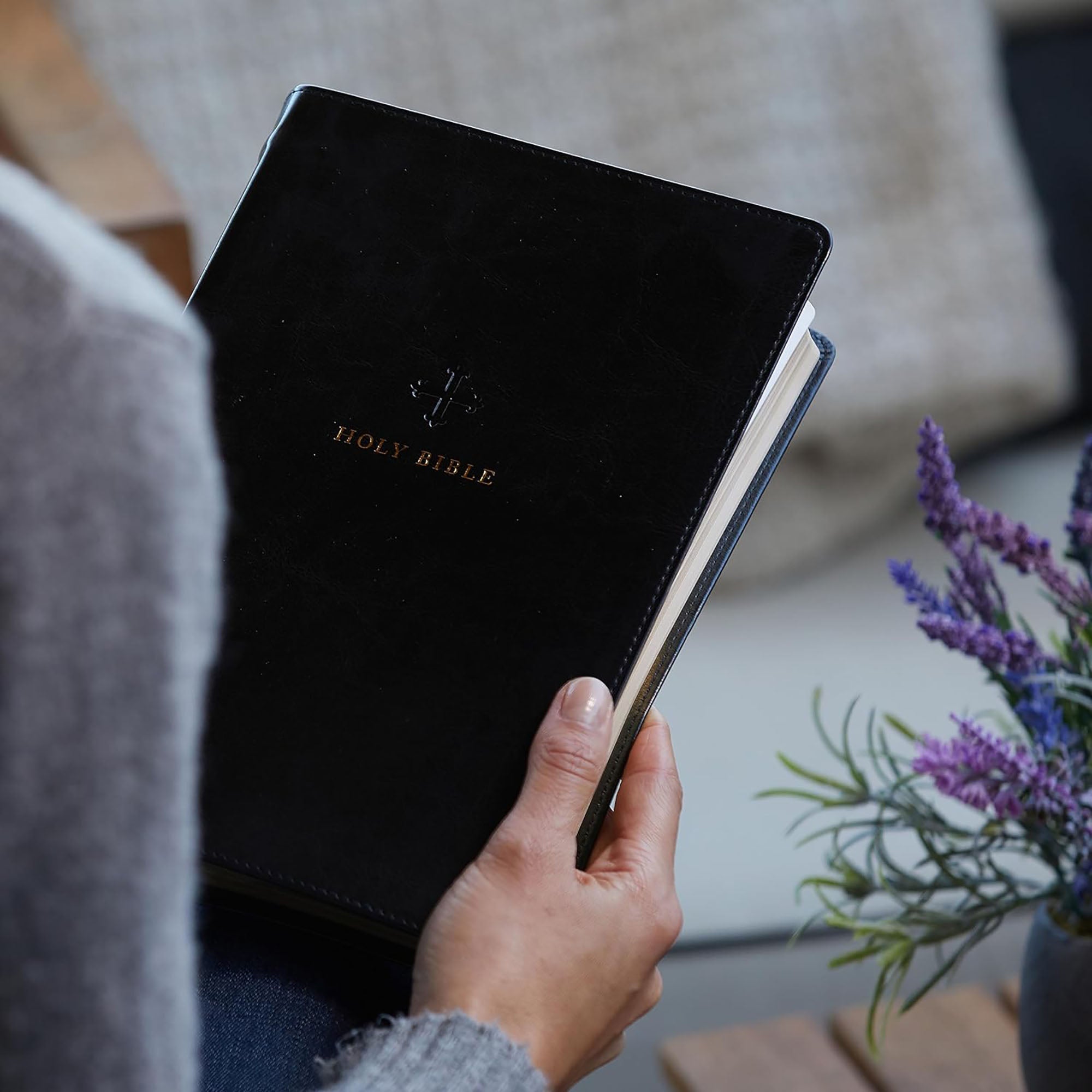 Black, faux-leather Holy Bible with gold lettering and simple cross design held by a woman.