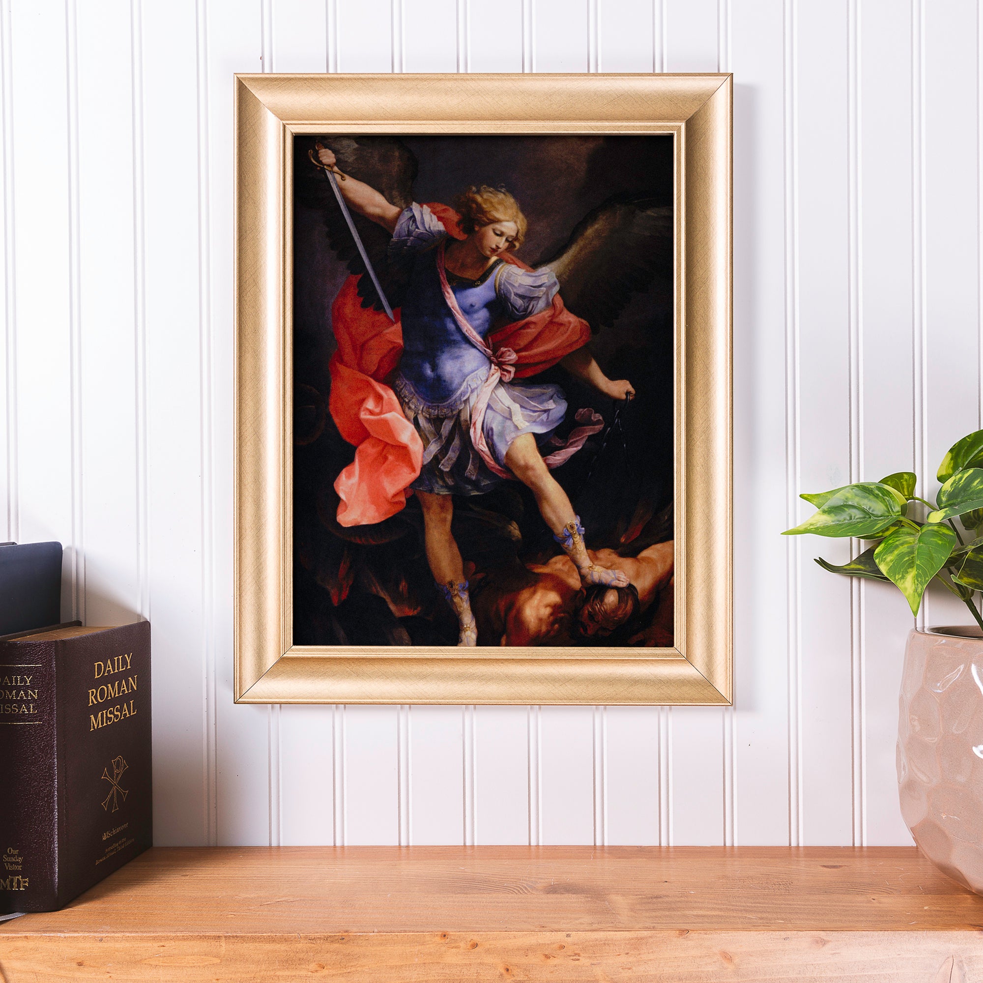 Framed "Saint Michael Defeating Satan" print with gold frame, depicting the biblical scene in an old master style.