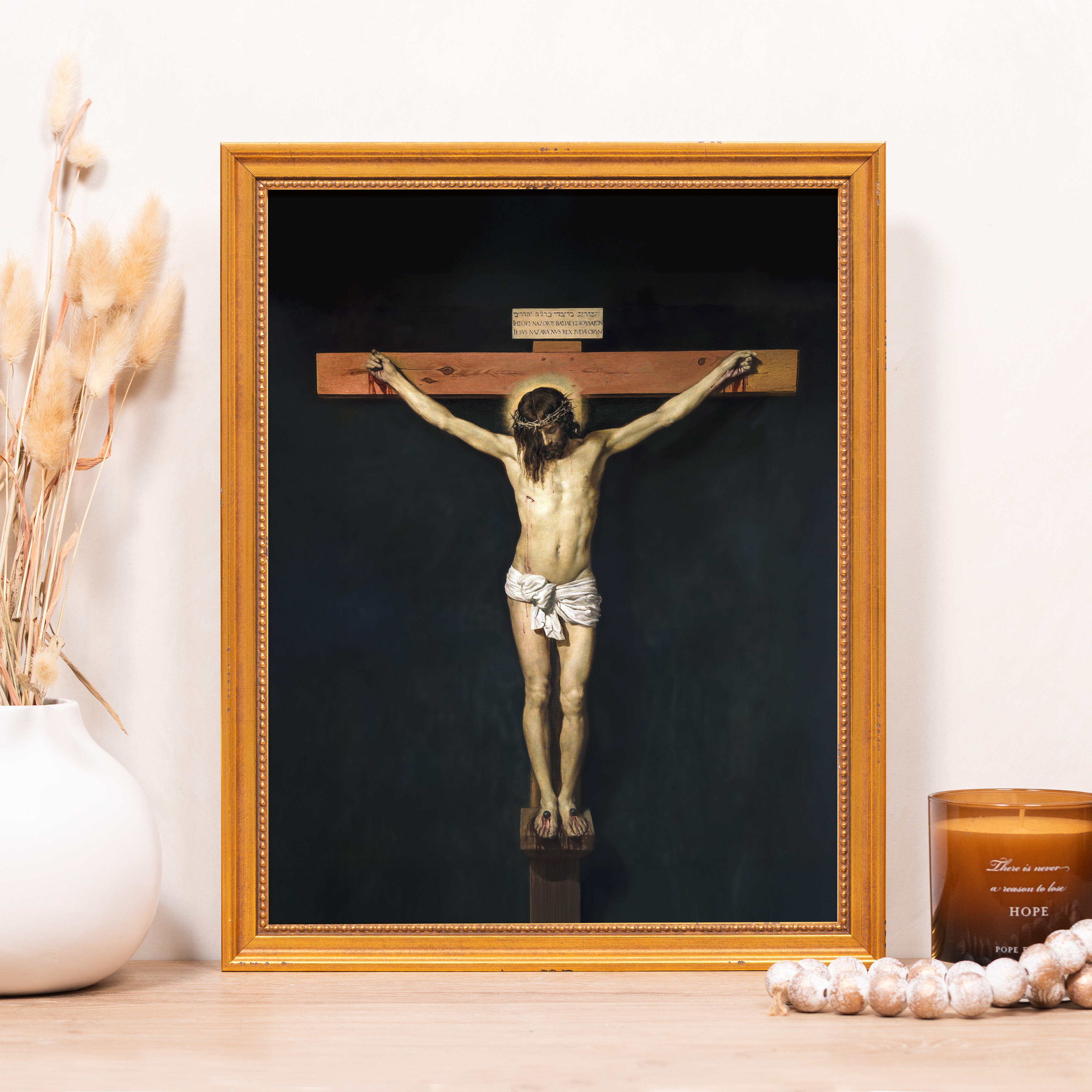 Crucifix artwork with a gold frame on a dark background; Jesus Christ is depicted on a wooden cross.