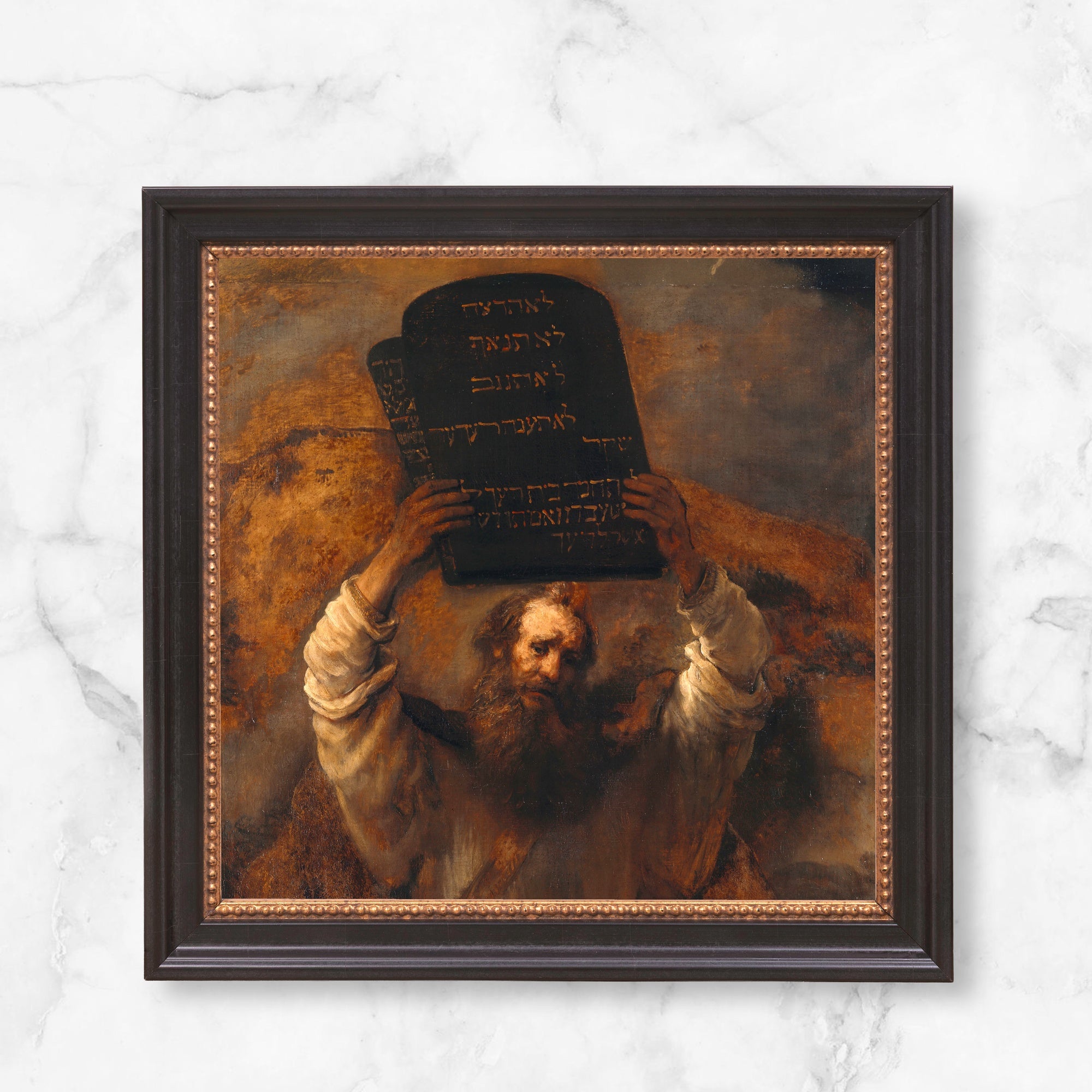 Framed painting of Moses holding the Ten Commandments with brown and black tones in a dark brown frame.