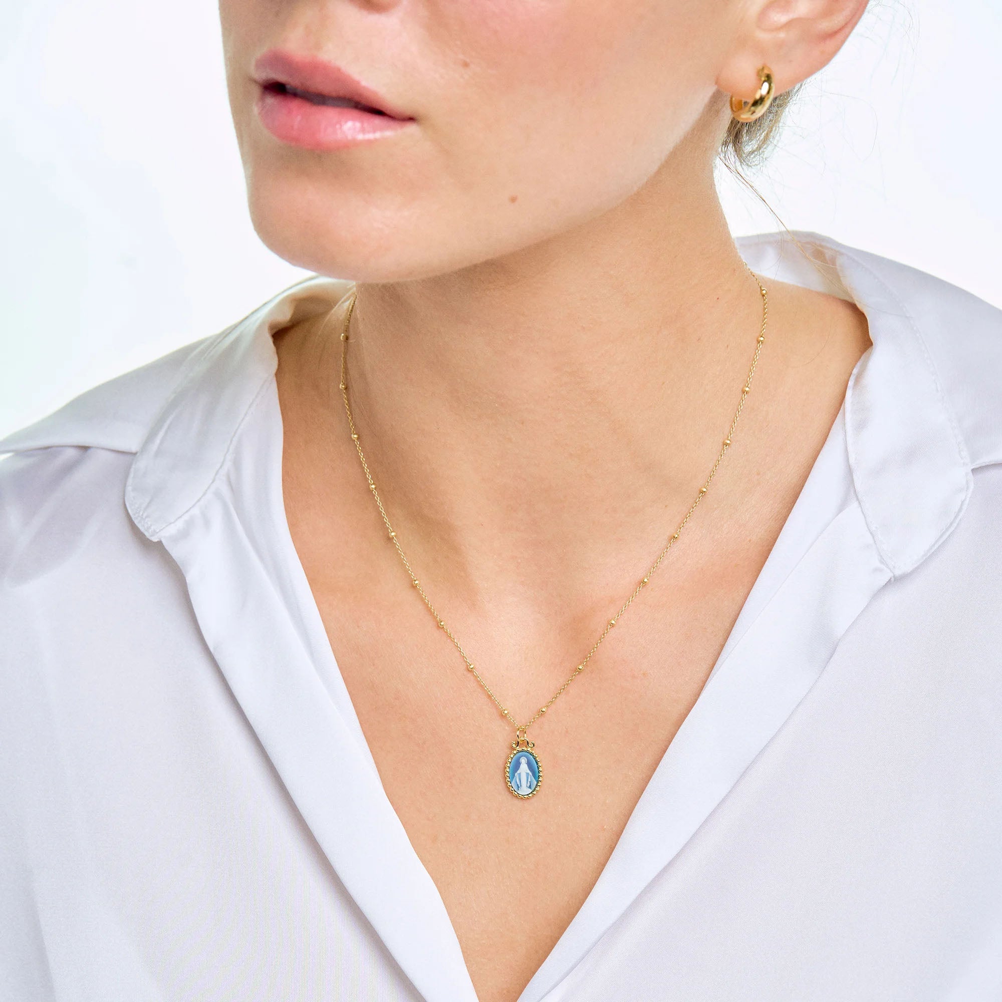 Necklace, Gold beaded chain with a blue Virgin Mary pendant.