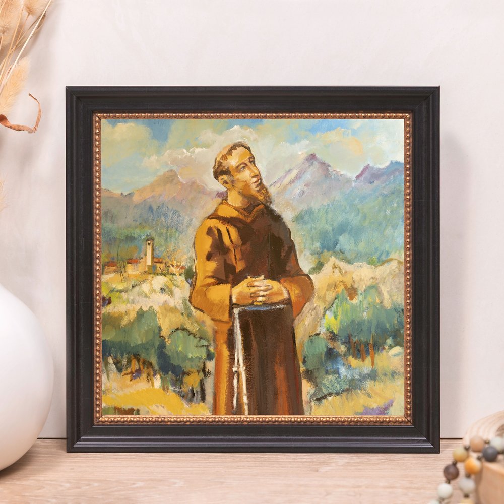 Framed painting of saint. Brown-robed man with beard gazes upwards; mountains, sky, and town are background; black frame.