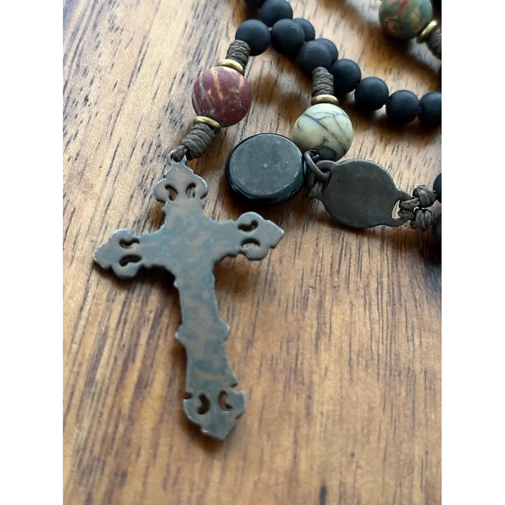 Close-up of a rosary with black beads and a metal cross on a wooden surface.