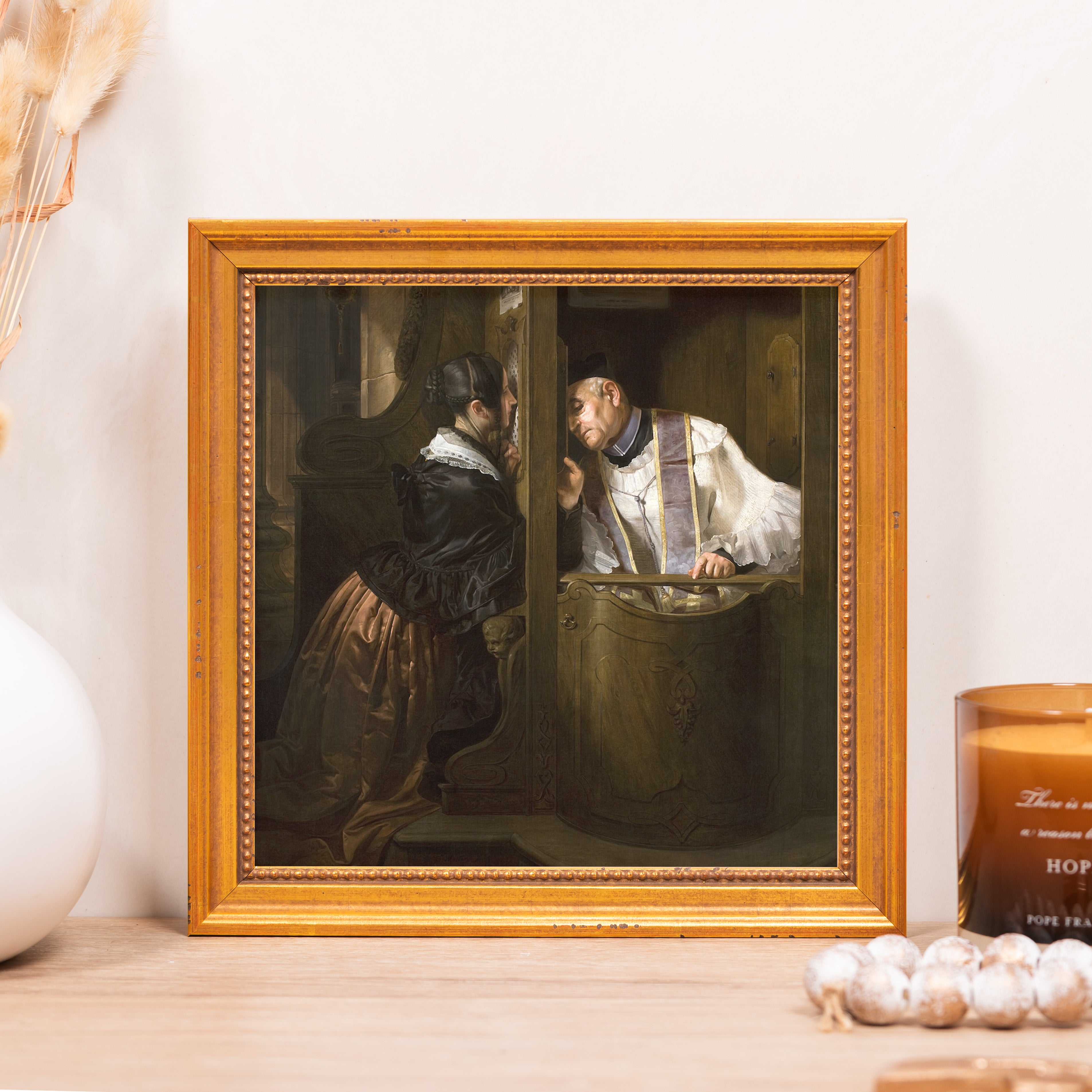 Framed print shows a priest hearing confession in gilded frame on a light wood surface.