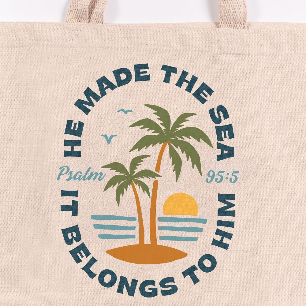 Beige canvas tote bag with a blue, yellow, and green palm tree design and the text "He made the sea and it belongs to him.".
