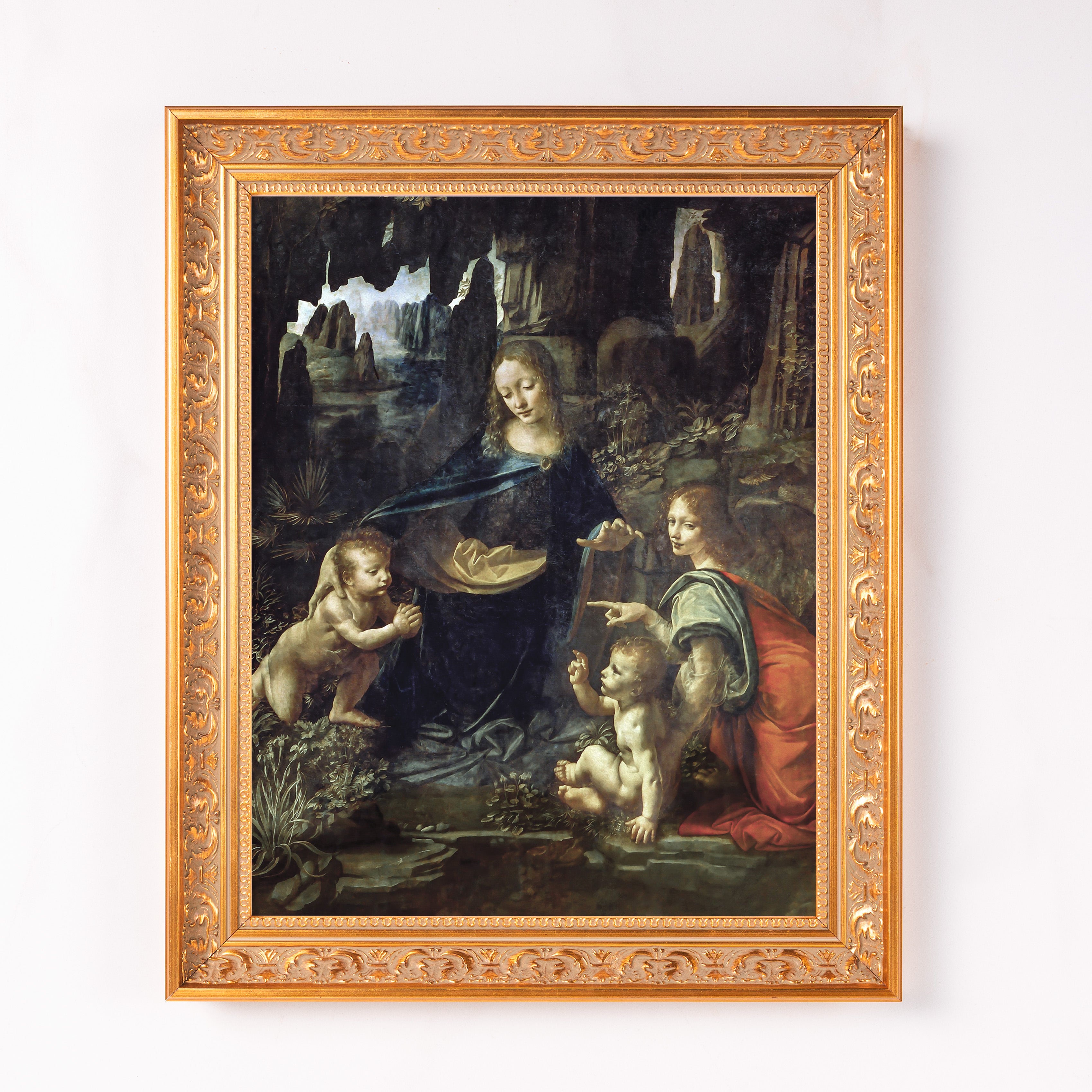 Framed Da Vinci's "Virgin of the Rocks" art print for wall decor in a decorative gold-colored frame and dark, painterly style.
