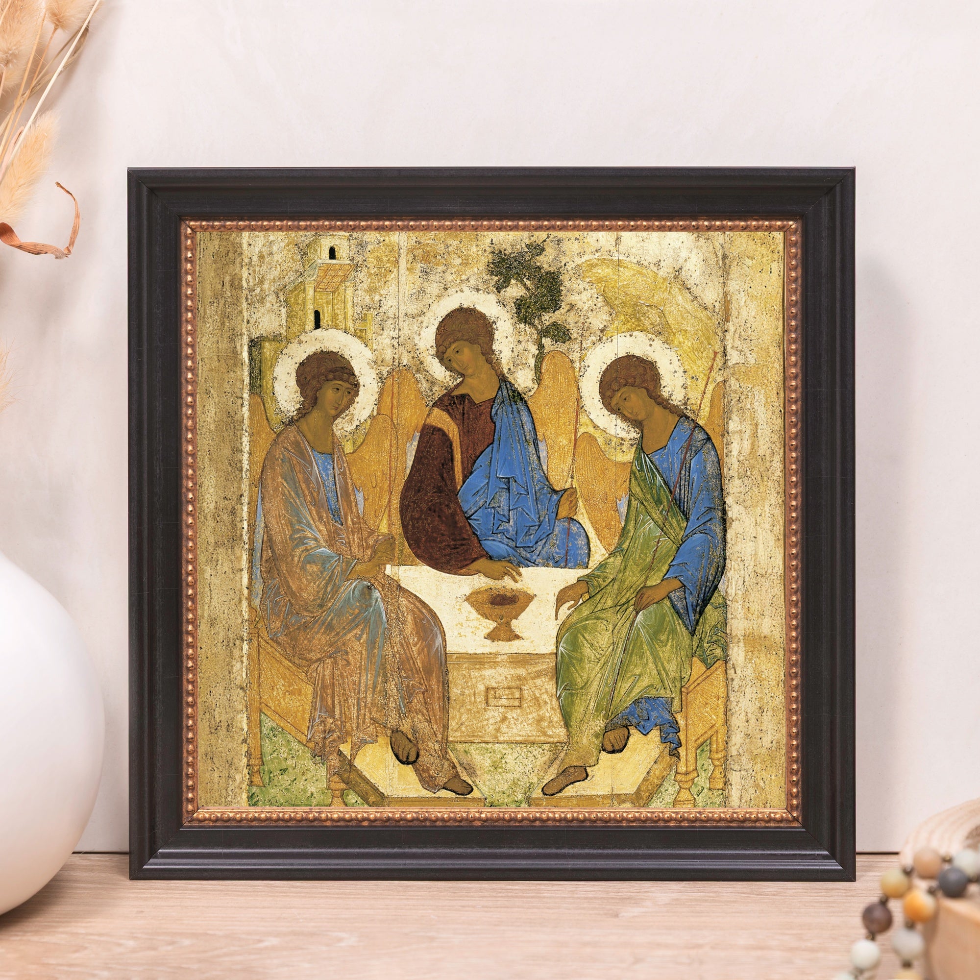Framed icon print depicting three haloed figures in blue, brown, and green robes sitting around a table.