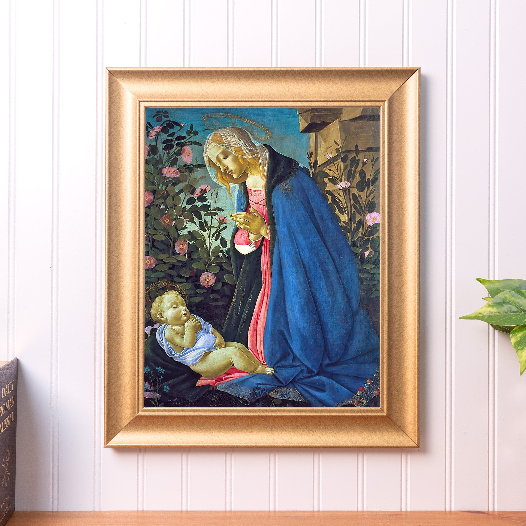 Framed painting of Mary and baby Jesus with a gold frame on a white wall.