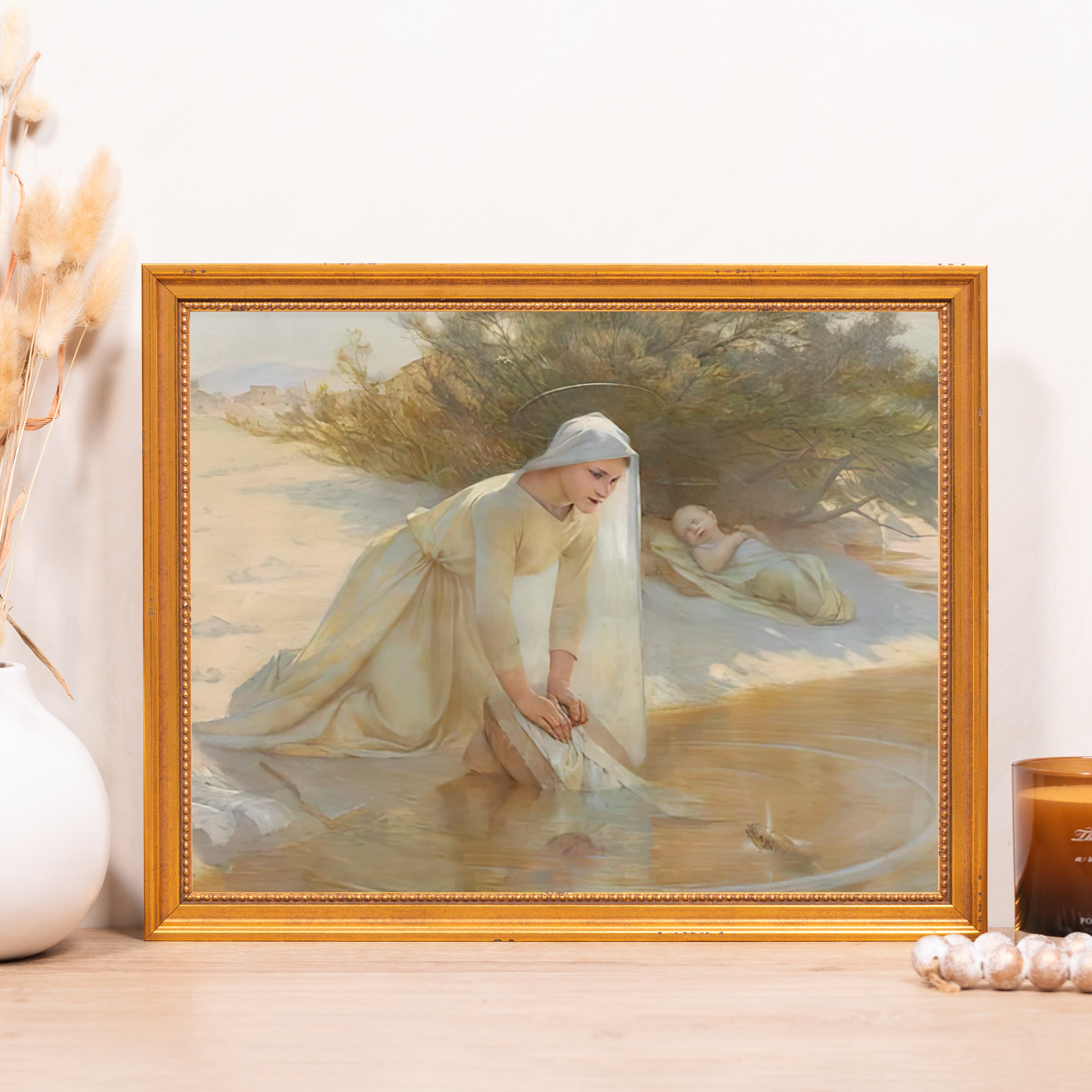 Framed art print showing woman washing clothes in water with sleeping child, in vintage style with a gold frame.
