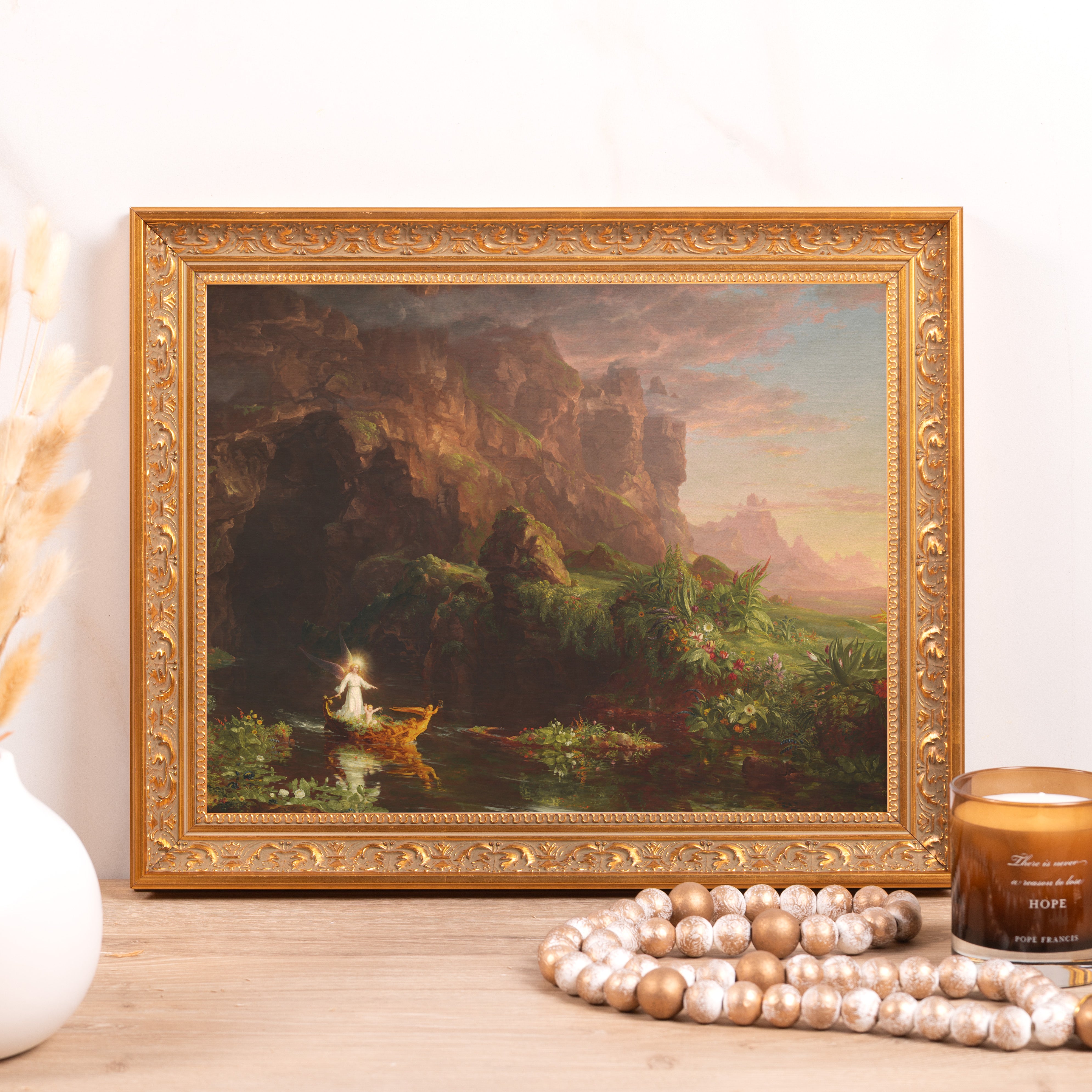 Framed landscape print features an angel in a boat on a river, ornate gold frame.