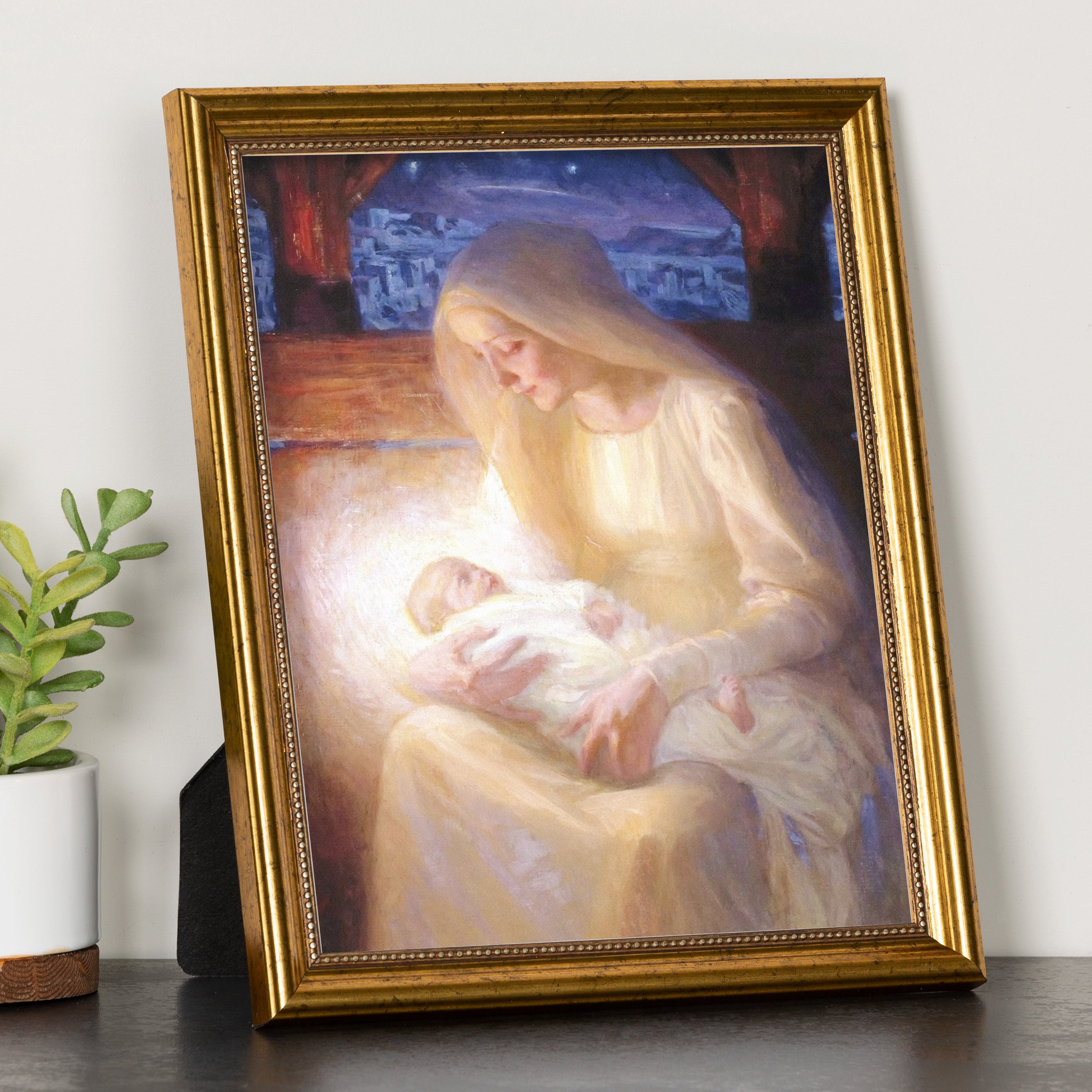 Framed art print depicting a pale Mary holding the baby Jesus, warm hues, gold frame.