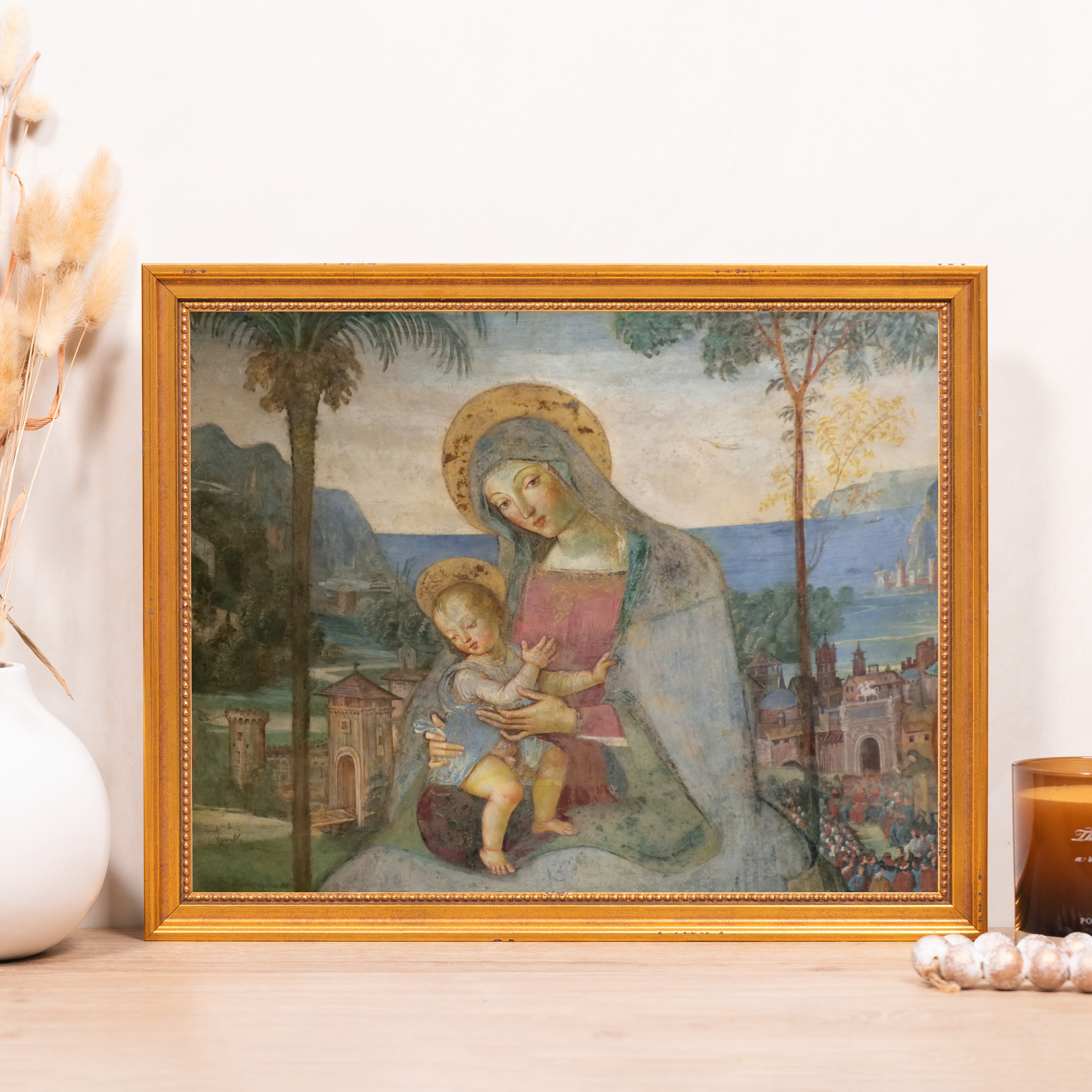 Framed print of Madonna and child in front of landscape with gold frame.