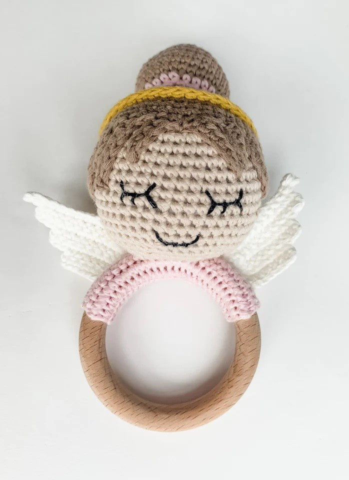 Angel-shaped baby rattle made of light brown crochet, with wings and a wooden handle.