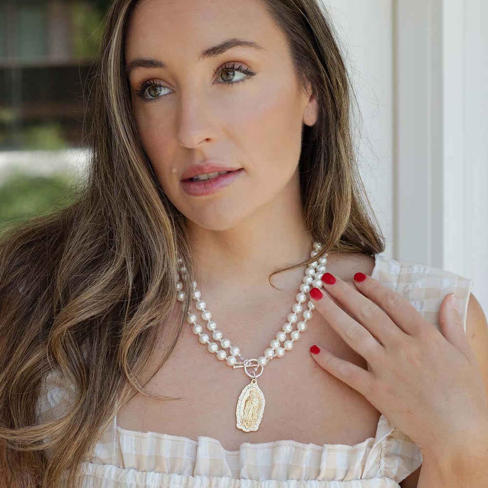 Necklace with a double strand of white pearls and an ornate gold Virgin Mary pendant.