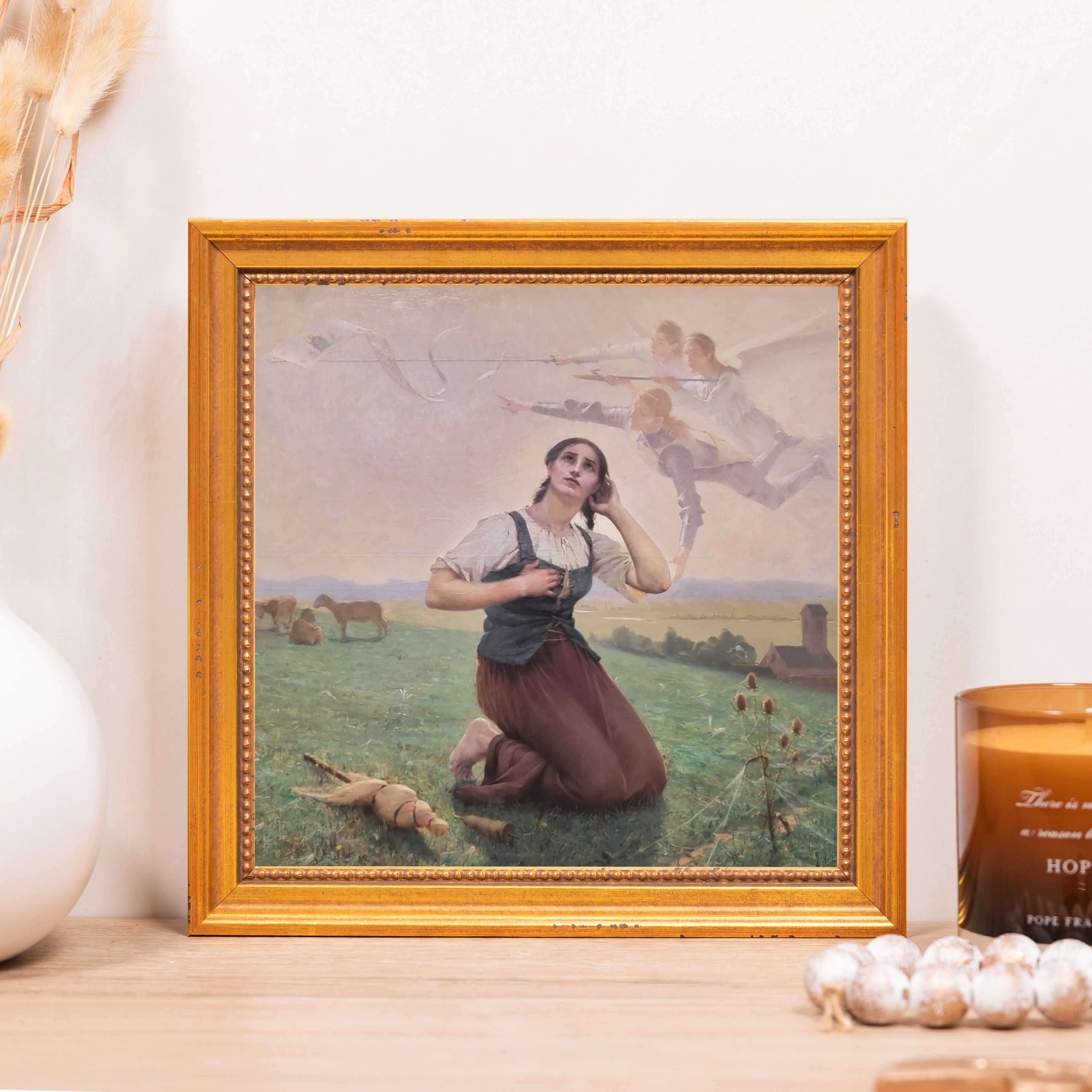Framed art print of Joan of Arc in brown and green with gold-colored ornate frame on wood table.