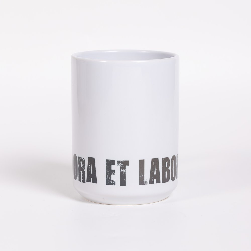 White, cylindrical ceramic mug with "Ora et Labora" in dark gray lettering.
