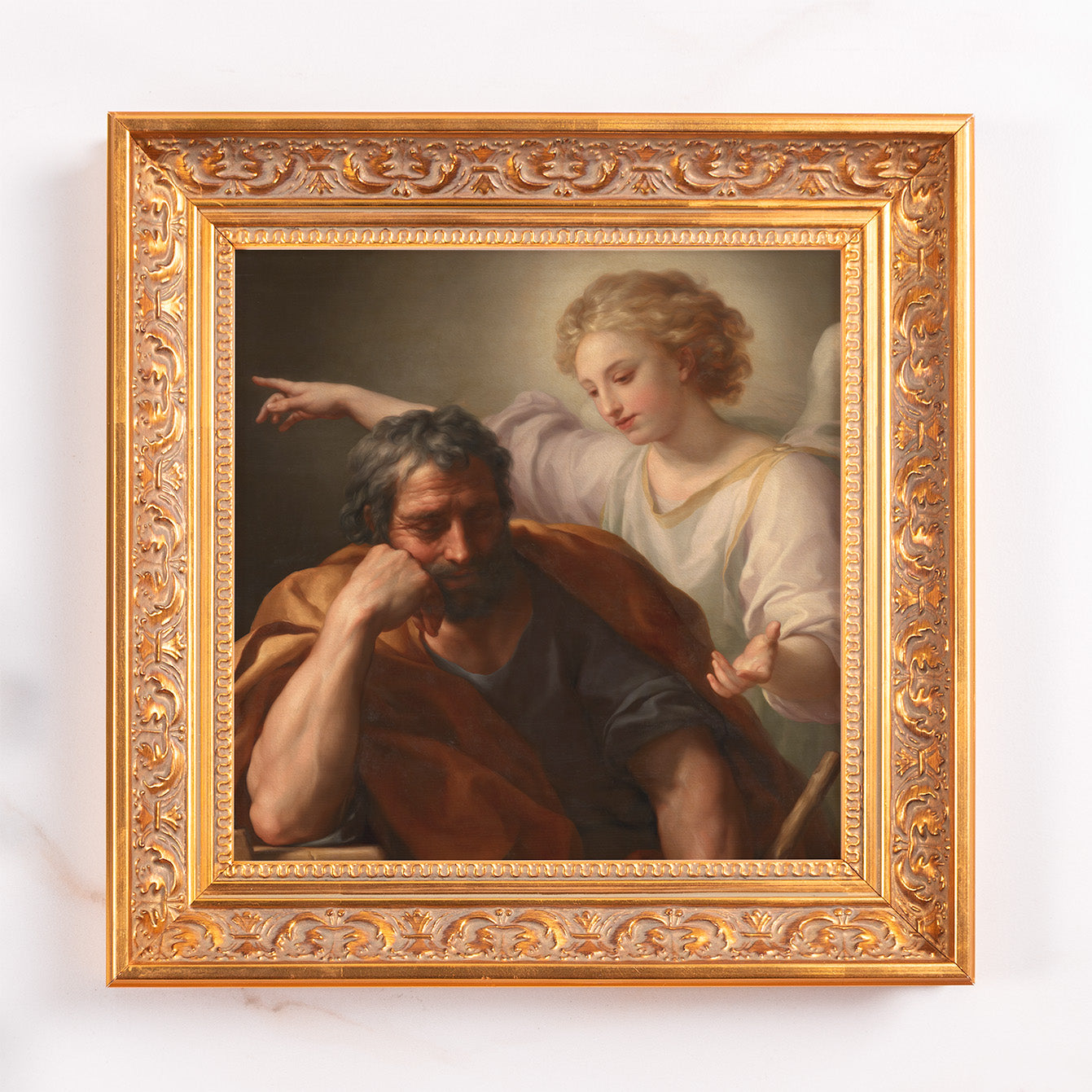 Framed oil painting of Joseph and an angel in ornate gold frame, on a white wall background.